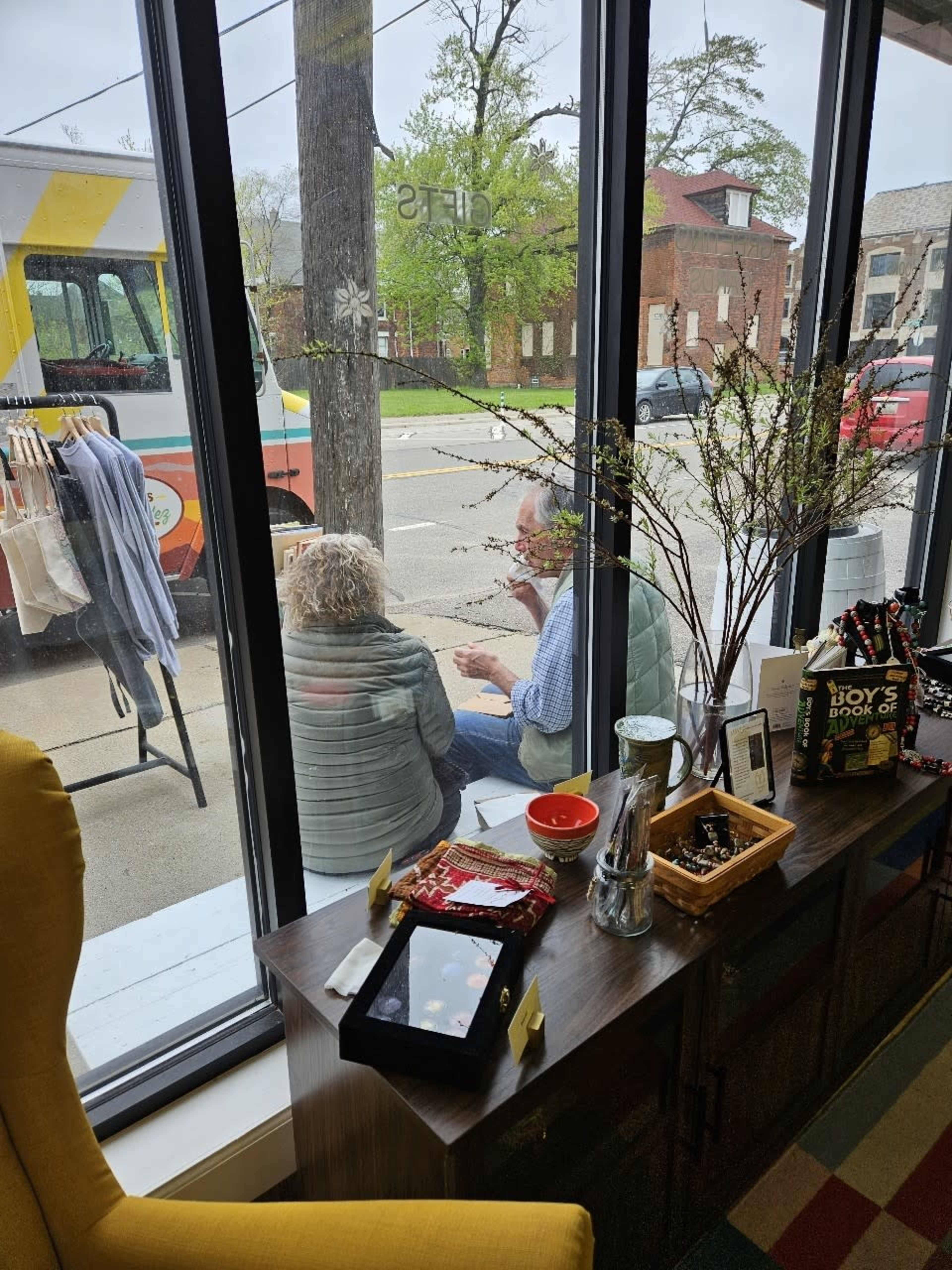 Two people sit outside a café, engaged in conversation, while a food truck is parked nearby.