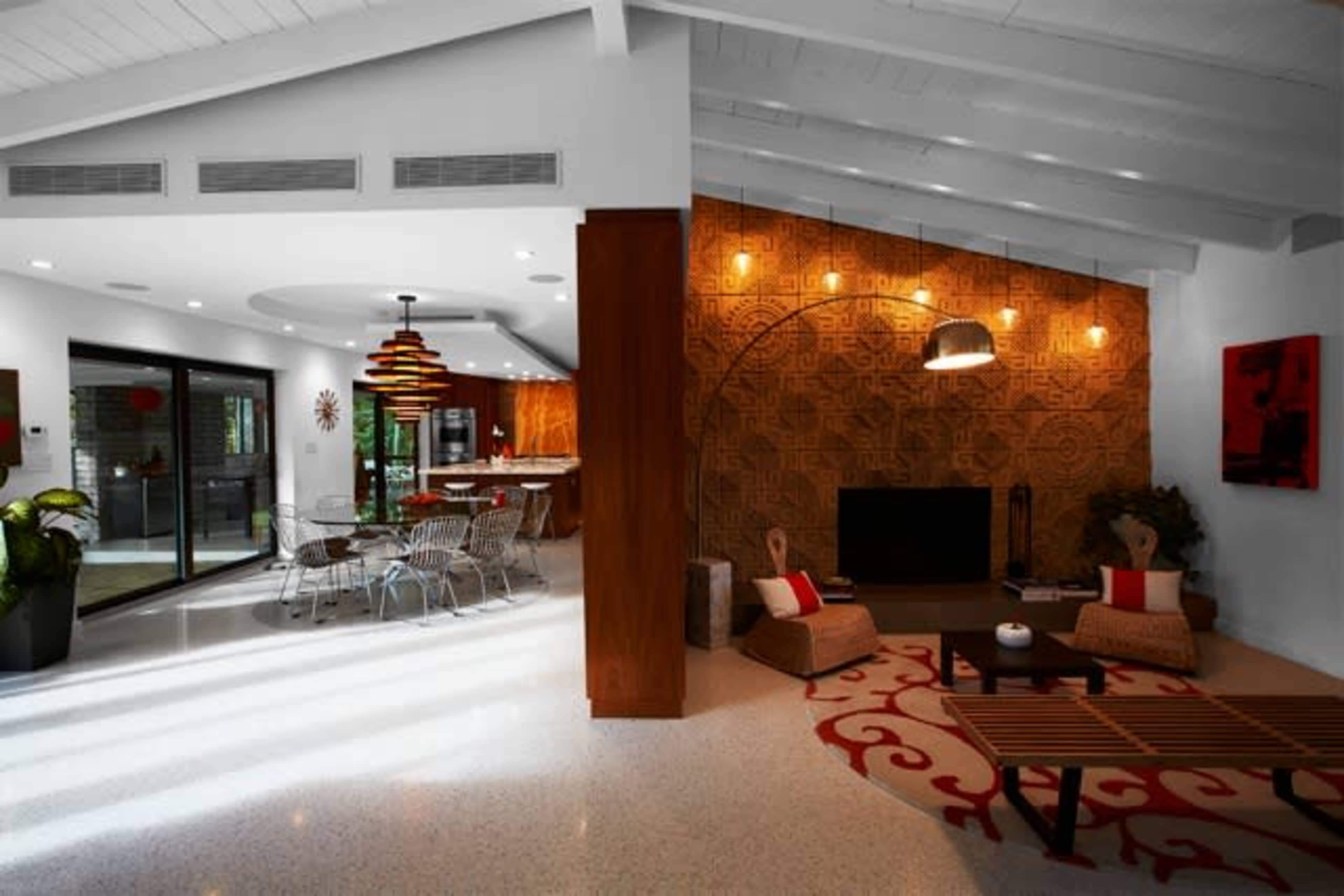 A modern living space featuring a dining area with a circular table, a wicker chair, and a patterned wall with a large floor lamp.