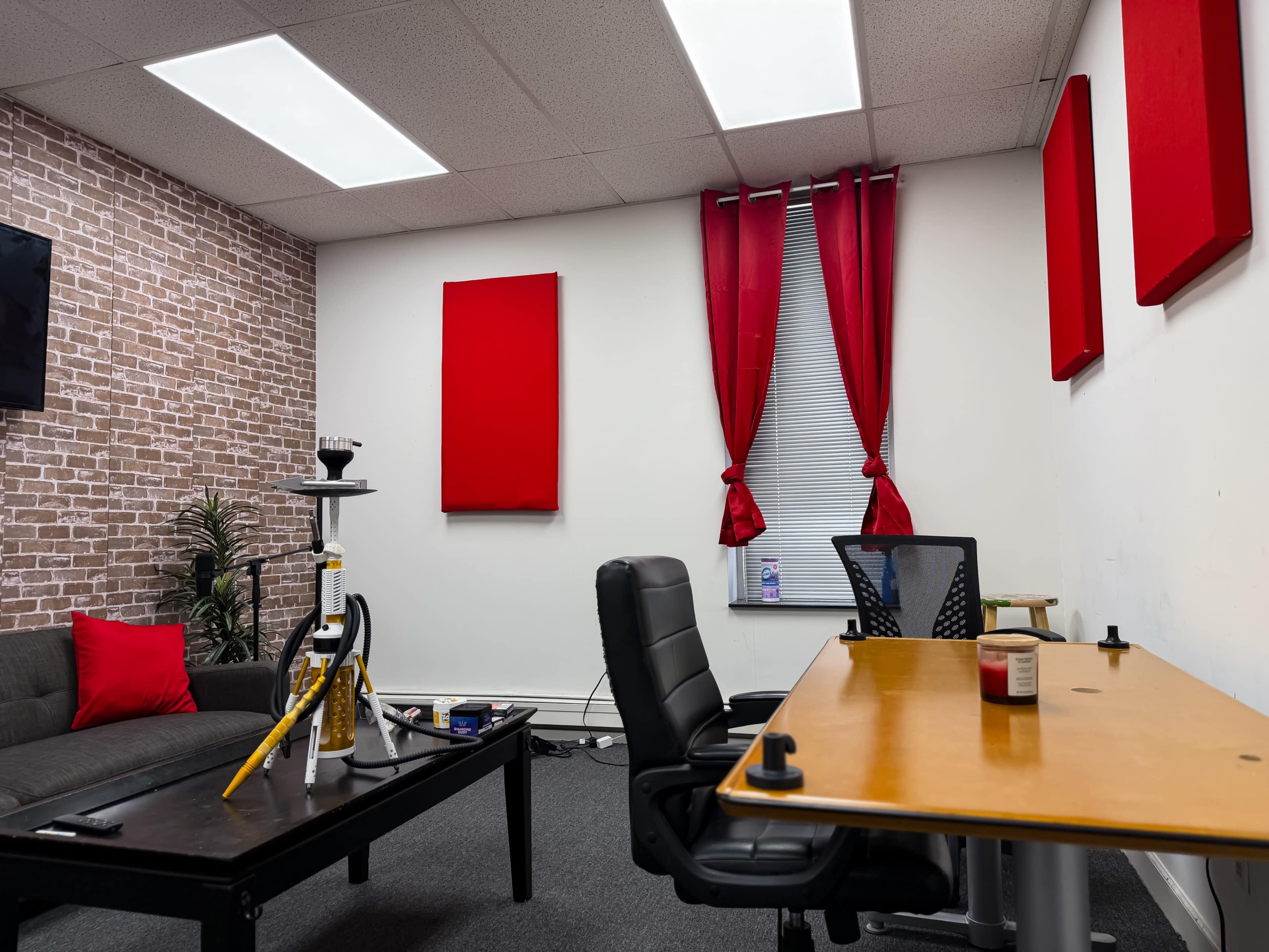 The image shows a small office space with a sofa, a coffee table, a desk with a chair, and red acoustic panels on the walls.