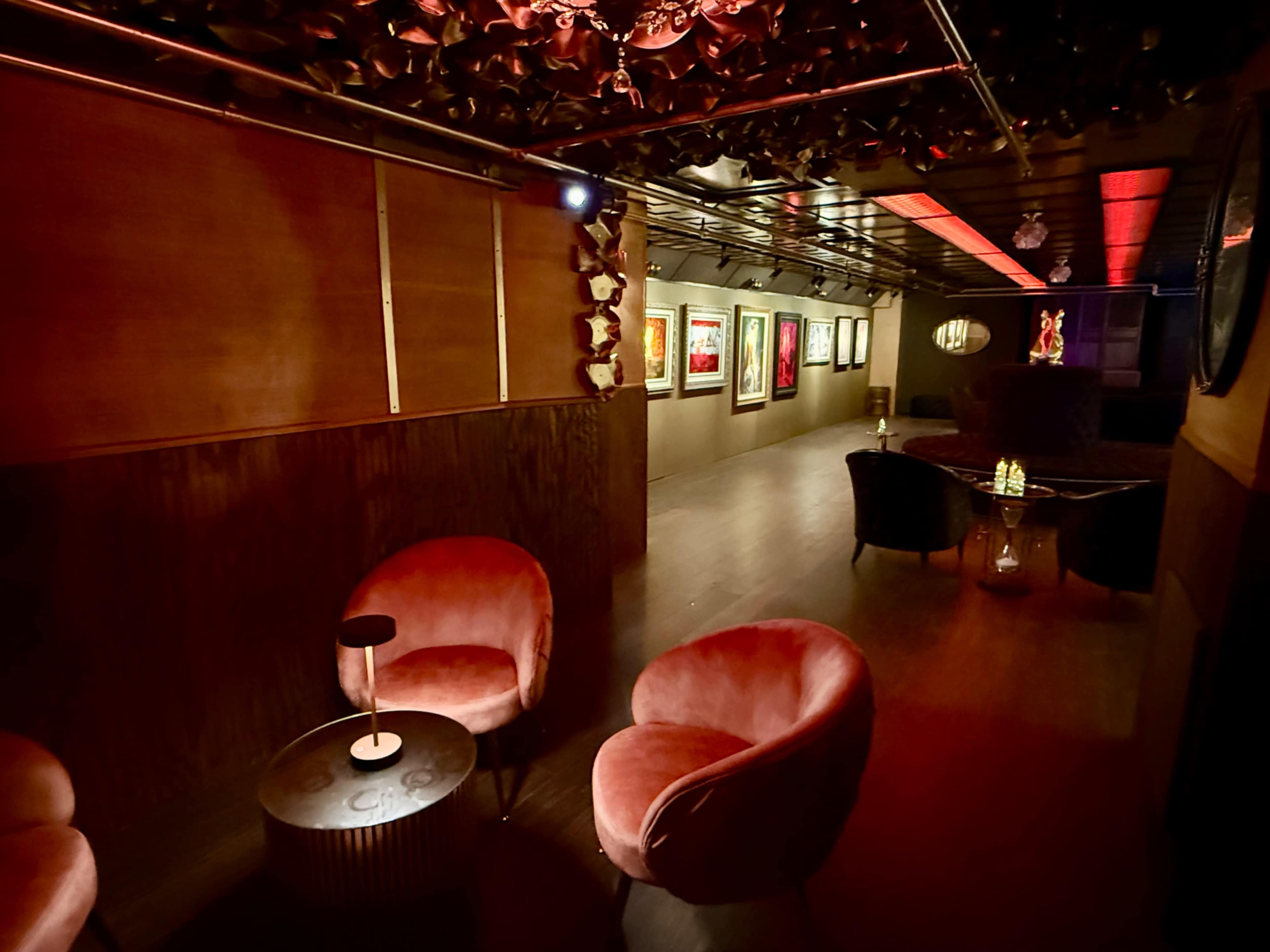 The image shows a dimly lit lounge area with plush seating and framed artwork on the walls.