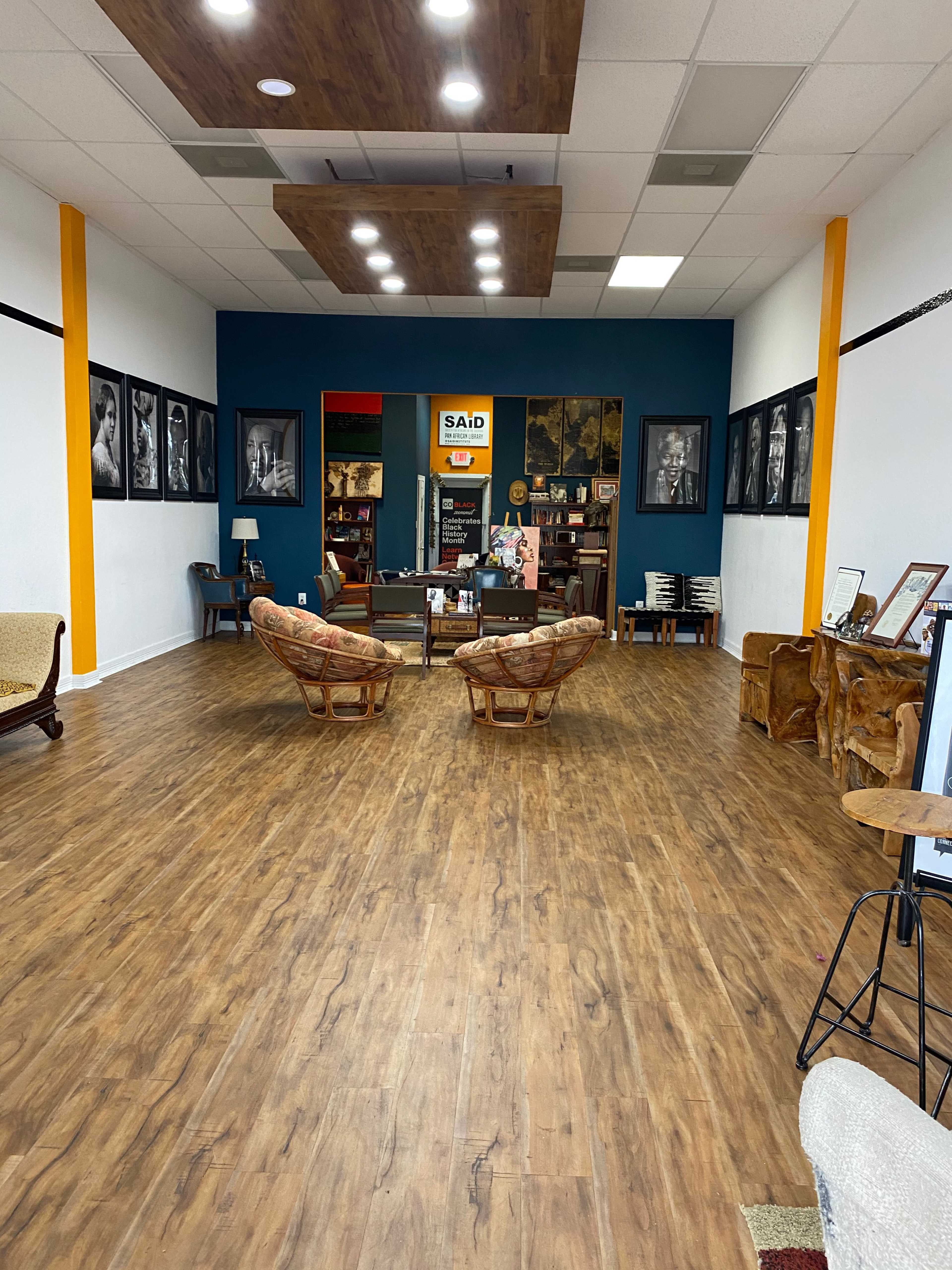 An interior space with wooden flooring, two patterned chairs facing each other, and framed black-and-white photographs lining the walls.
