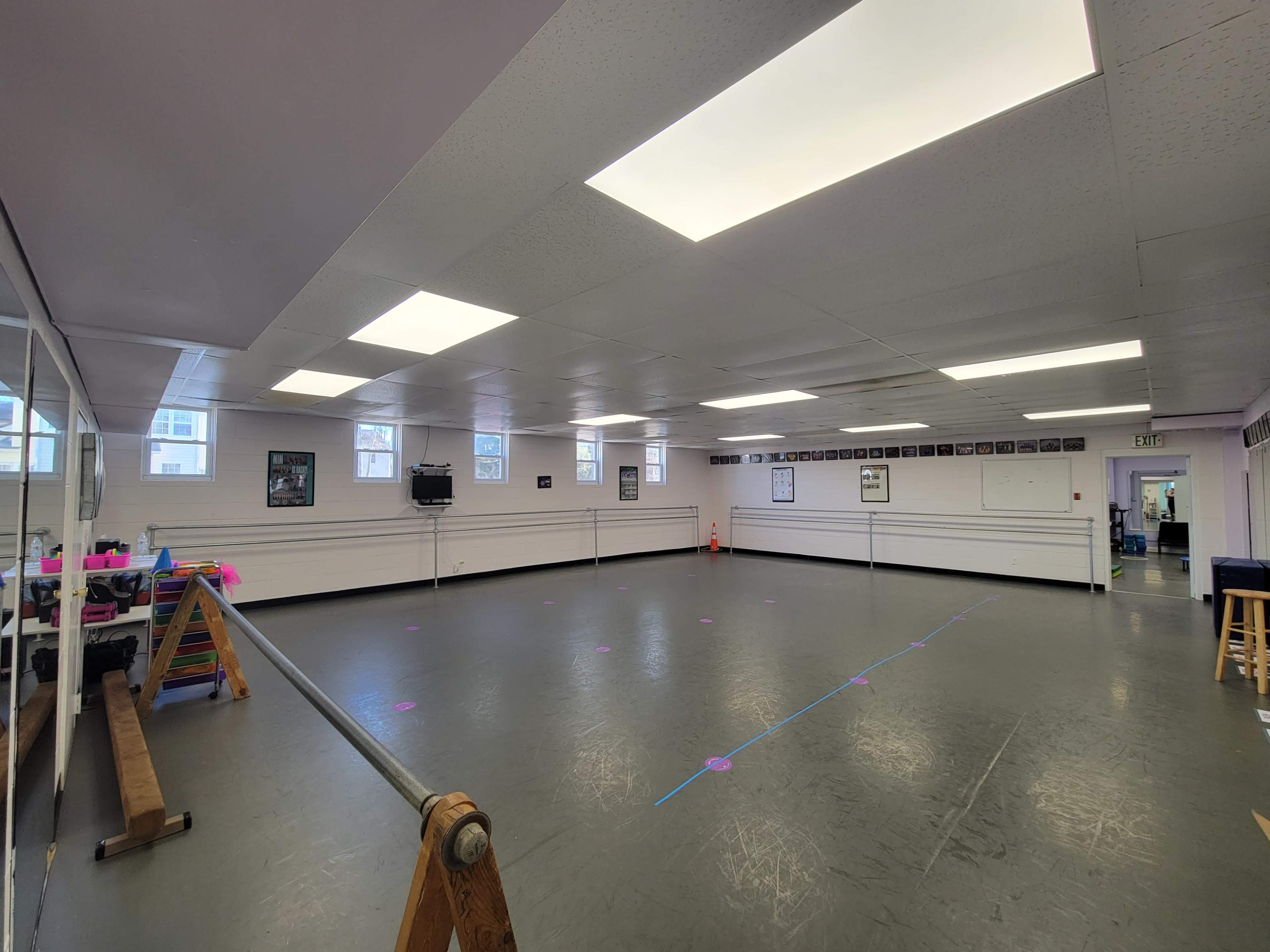 A large, empty dance studio with mirrors on one wall and fluorescent lighting overhead.