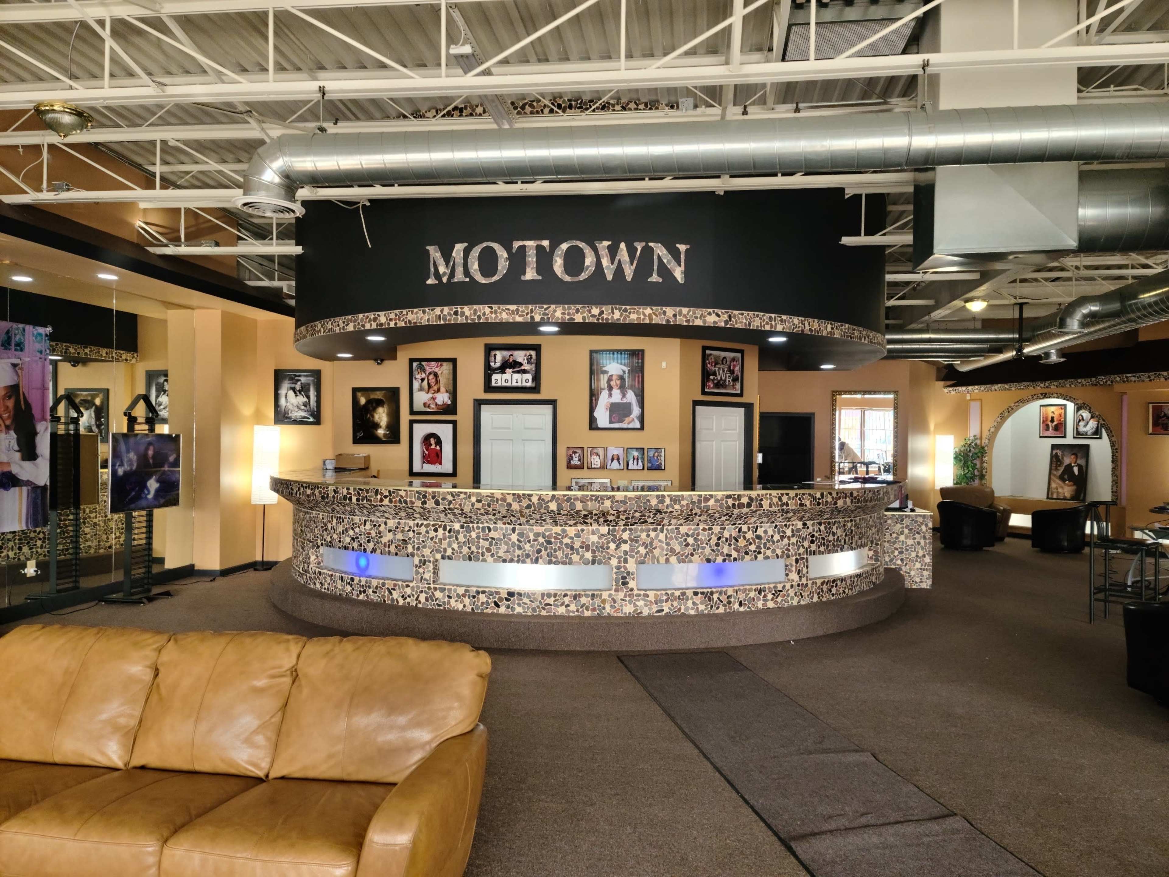 The image shows a reception area with a curved counter labeled "MOTOWN," surrounded by framed photographs and a leather sofa nearby.