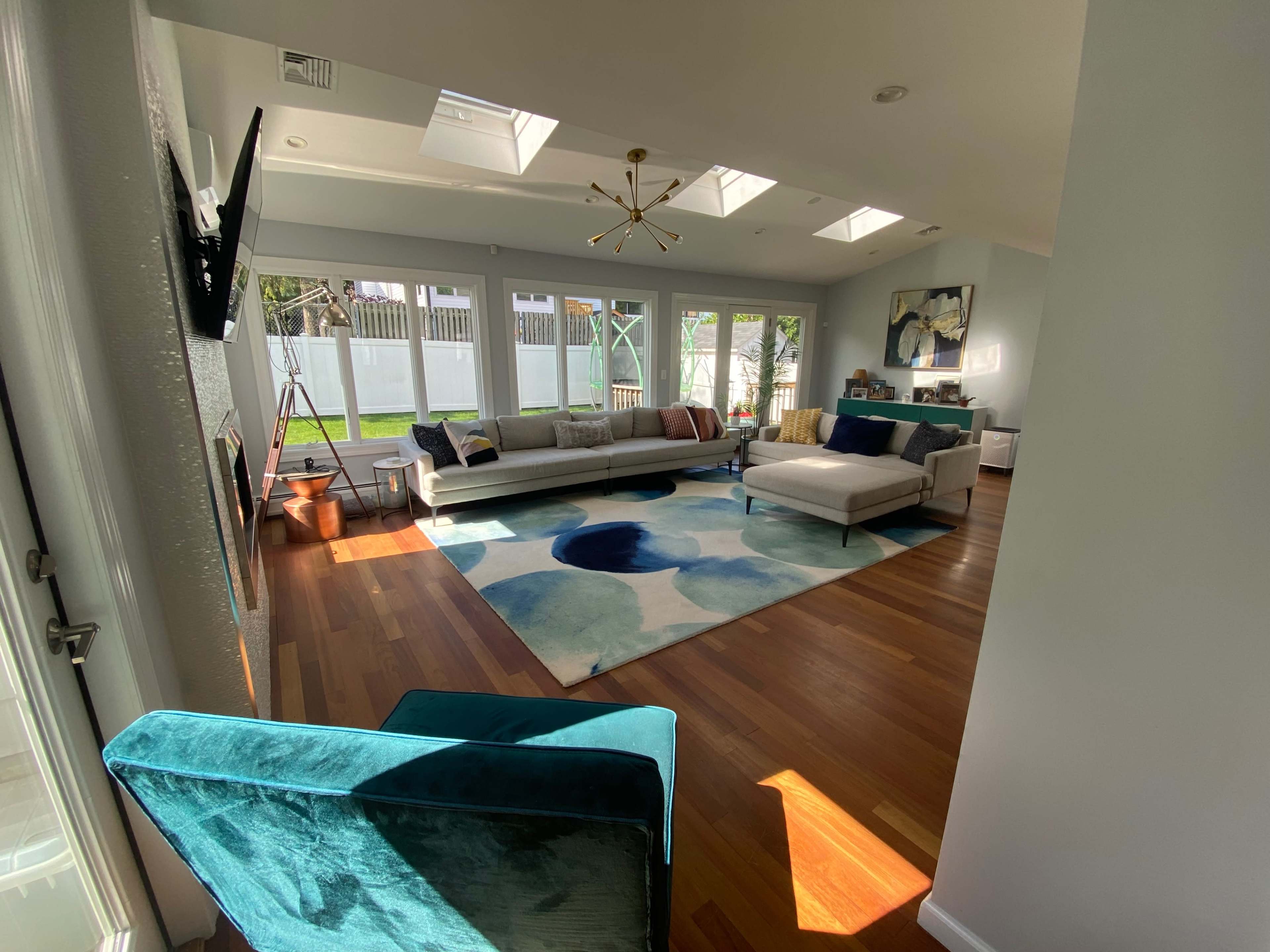 A spacious living room with large windows, a soft area rug featuring a colorful design, and a sectional sofa arranged around a central coffee table.