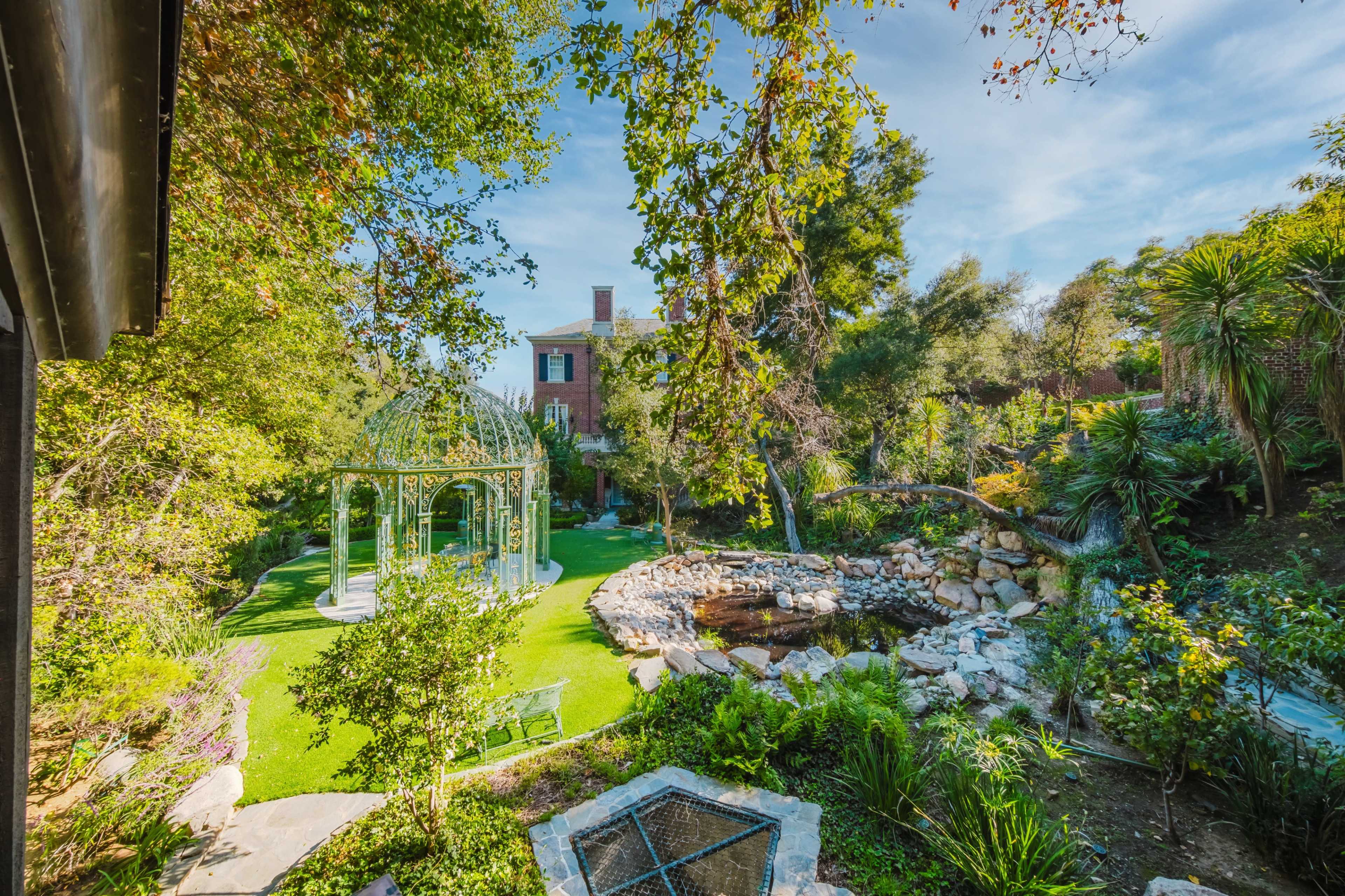 The image shows a well-maintained garden featuring a gazebo, a pond, and various trees and plants.