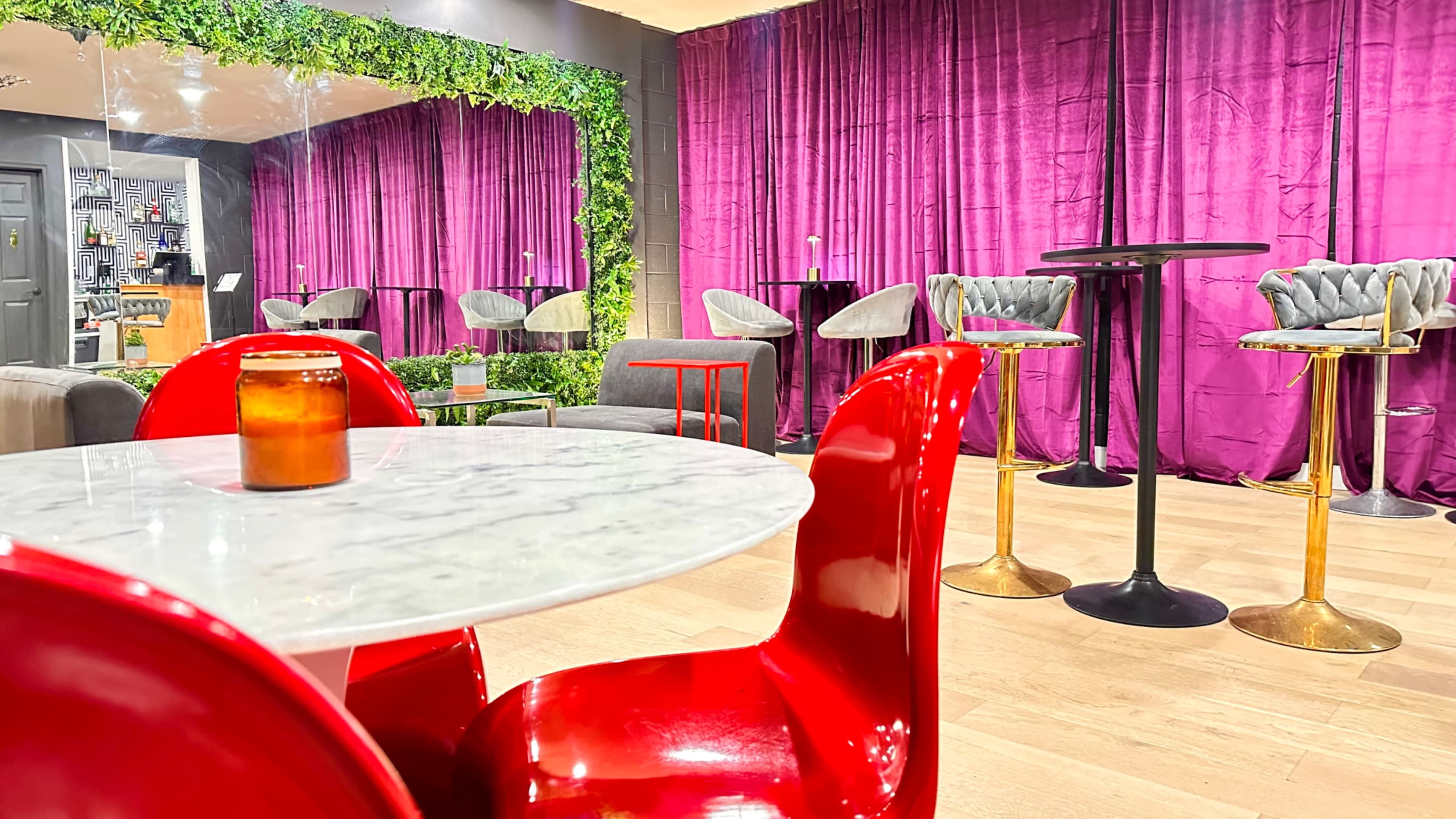 The image shows a modern interior space featuring red chairs around a marble table, with purple curtains and various seating arrangements in the background.