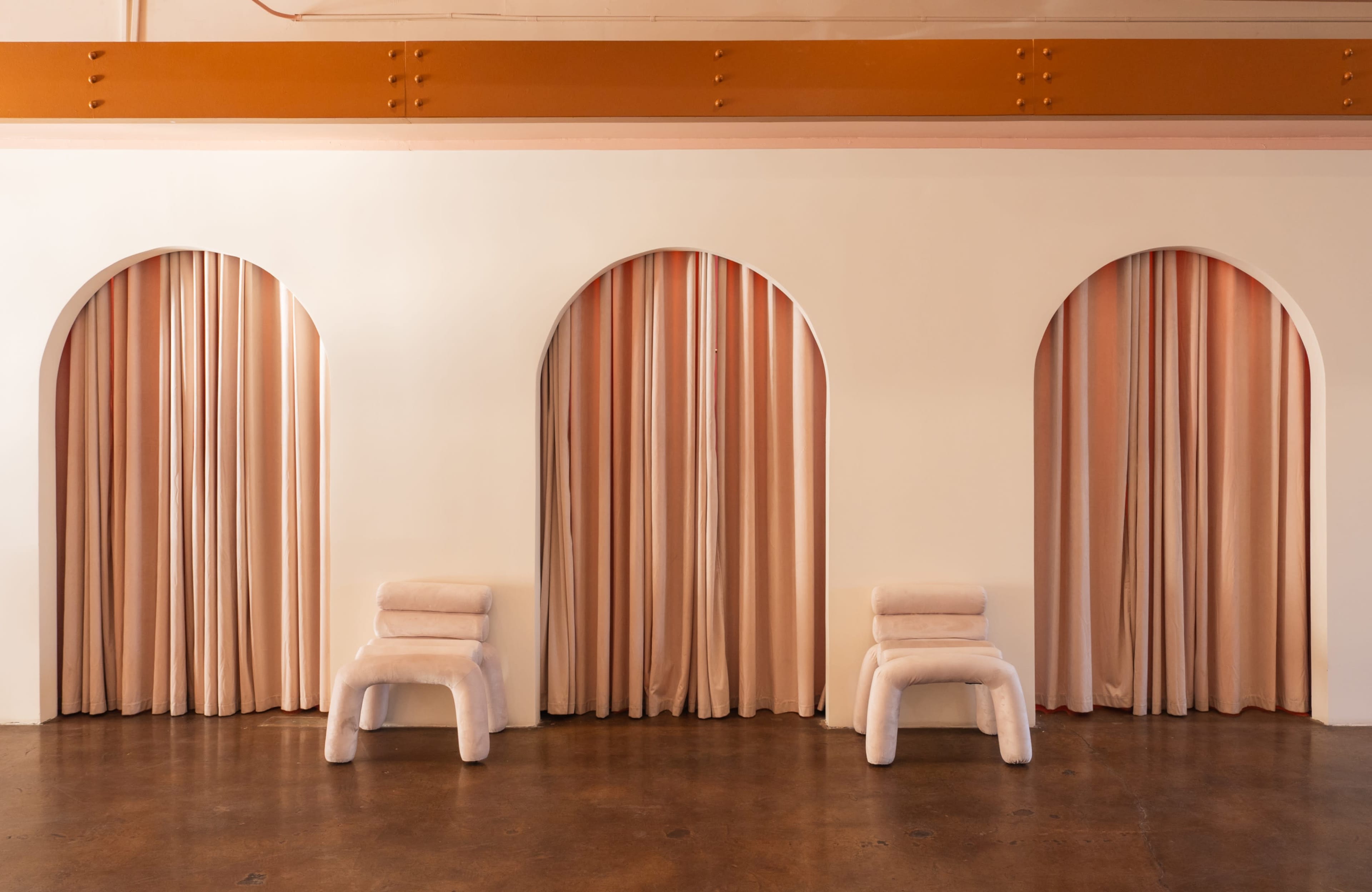 The image shows three archways with light pink curtains, flanked by two white, plush seating arrangements on a hardwood floor.