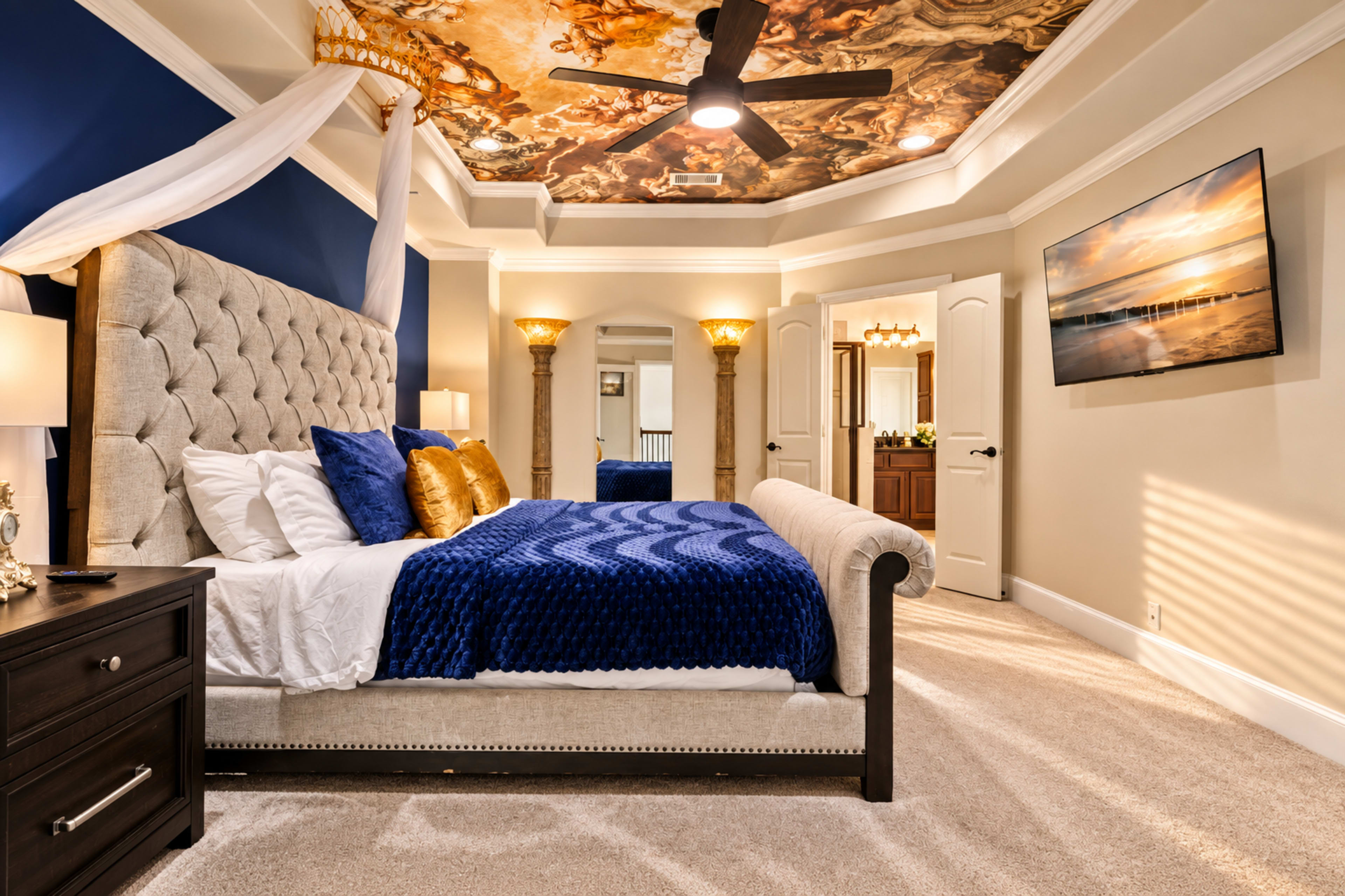 The image shows a luxurious bedroom featuring a tufted bed with blue and gold accents, a decorative ceiling, and a wall-mounted TV.