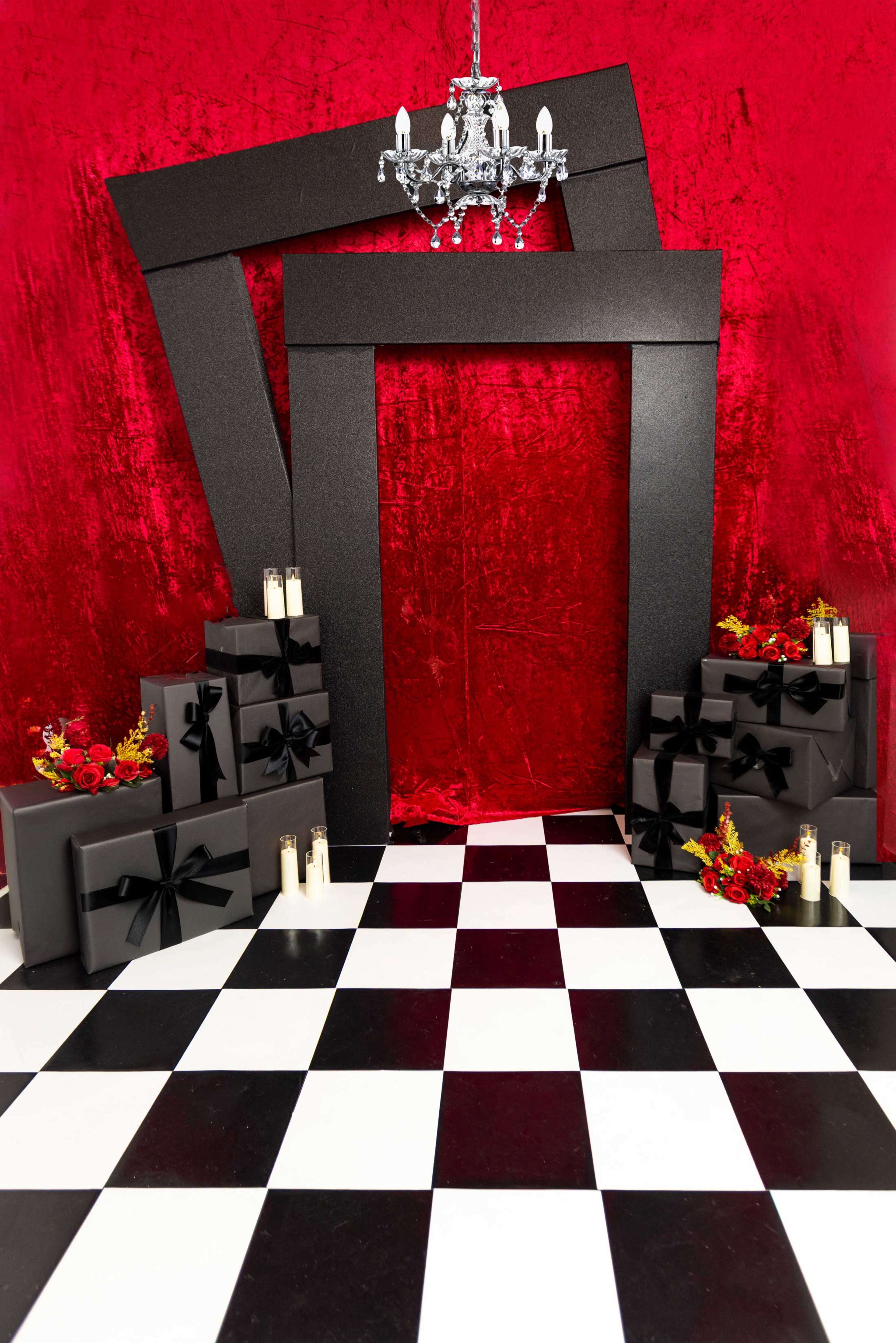 The scene features a staged area with a large black frame, gift boxes wrapped in black with bows, candles, and a red backdrop with a checkerboard floor.