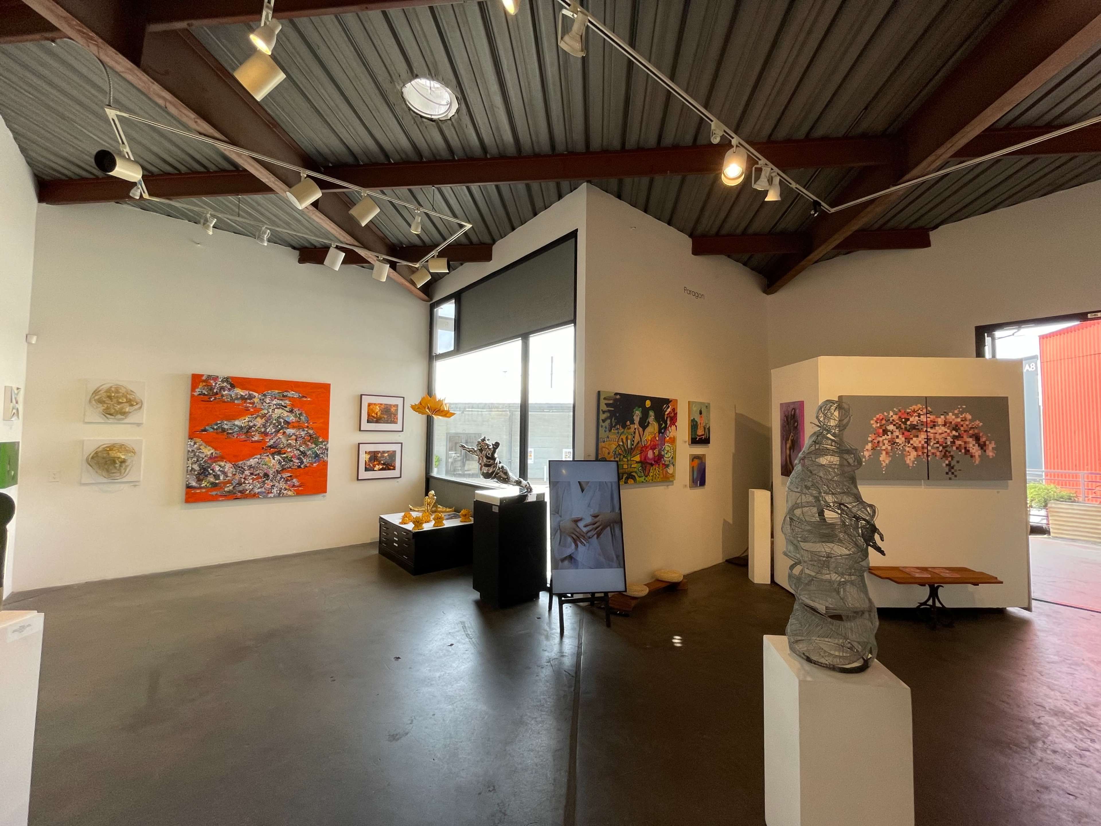 A modern art gallery featuring various colorful artworks on the walls, a sculpture in the center, and a display of objects on a table.