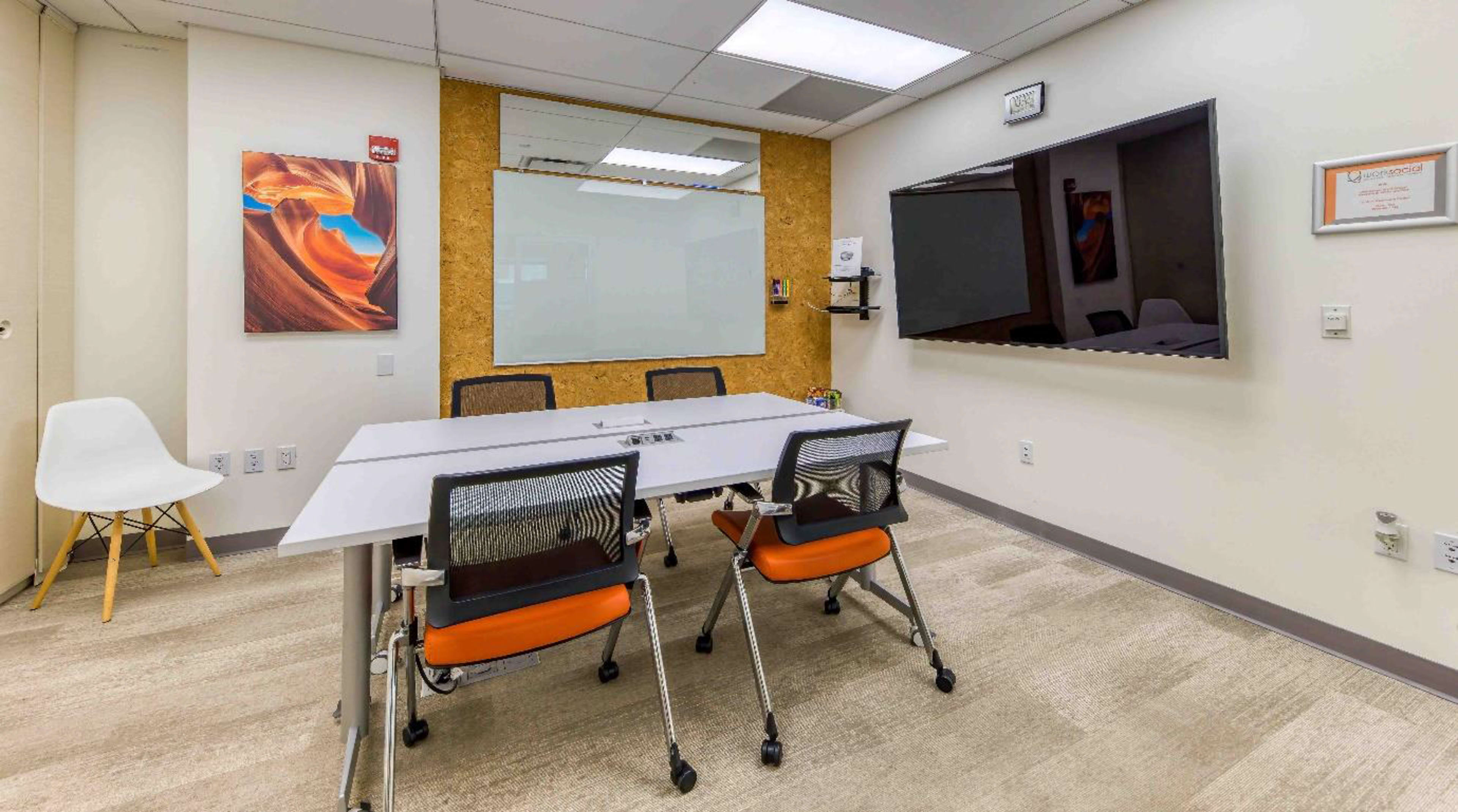 A modern conference room featuring a rectangular table surrounded by four chairs, a wall-mounted screen, and a large whiteboard.