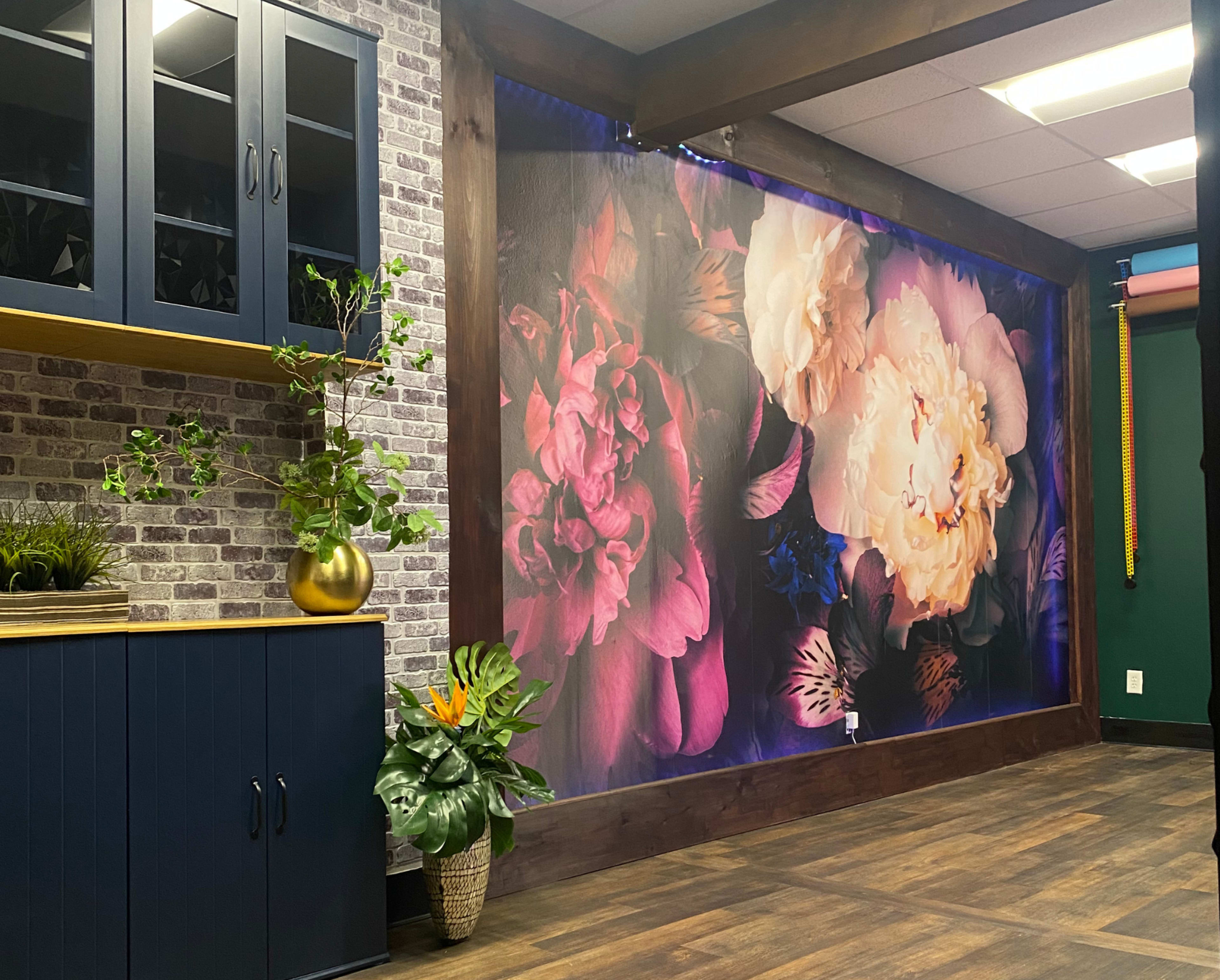 The image shows a room featuring a large floral mural on one wall, accompanied by a dark blue cabinet and decorative plants.
