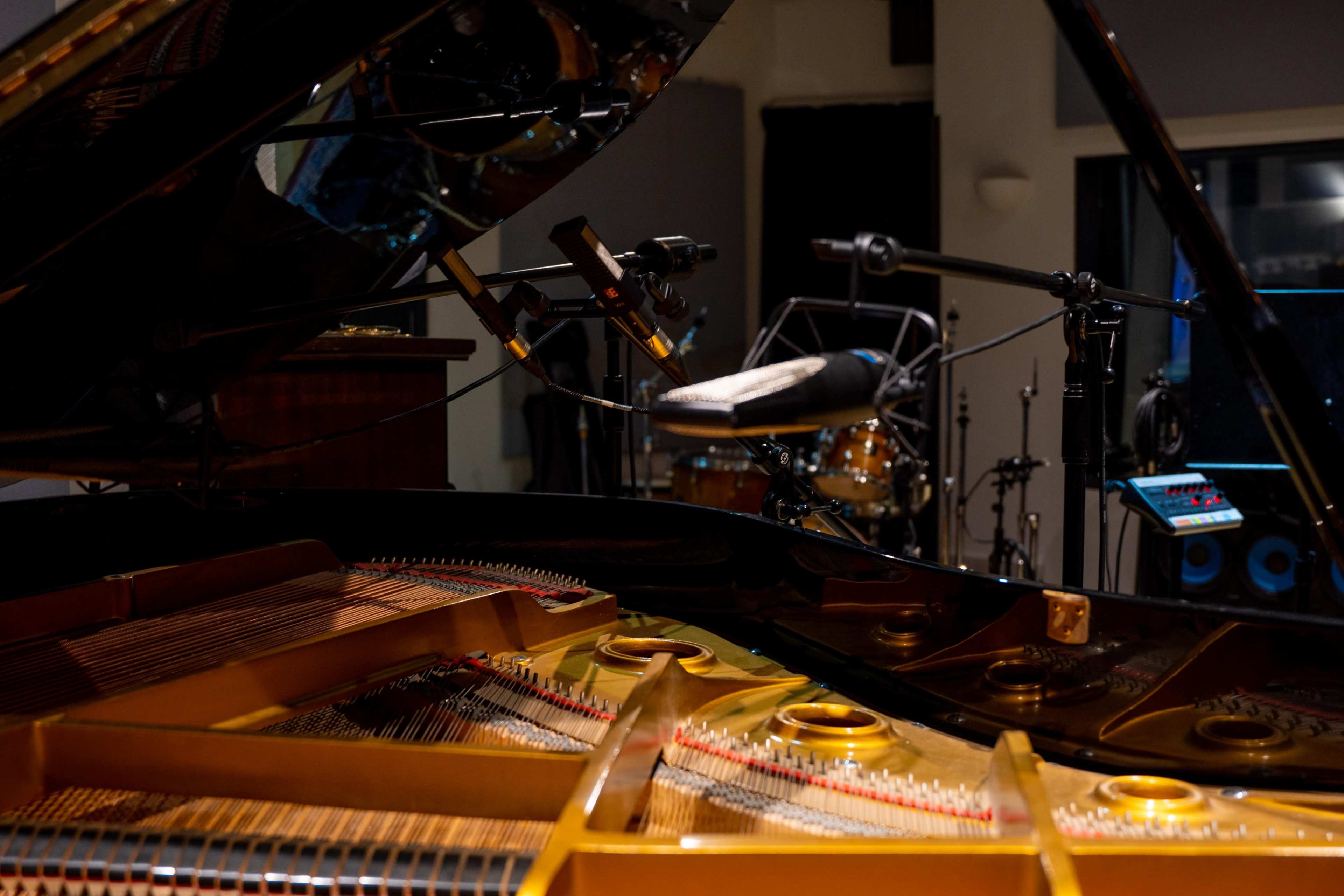 The image shows a close-up view of the interior of a grand piano with microphones positioned nearby, set in a music studio environment.
