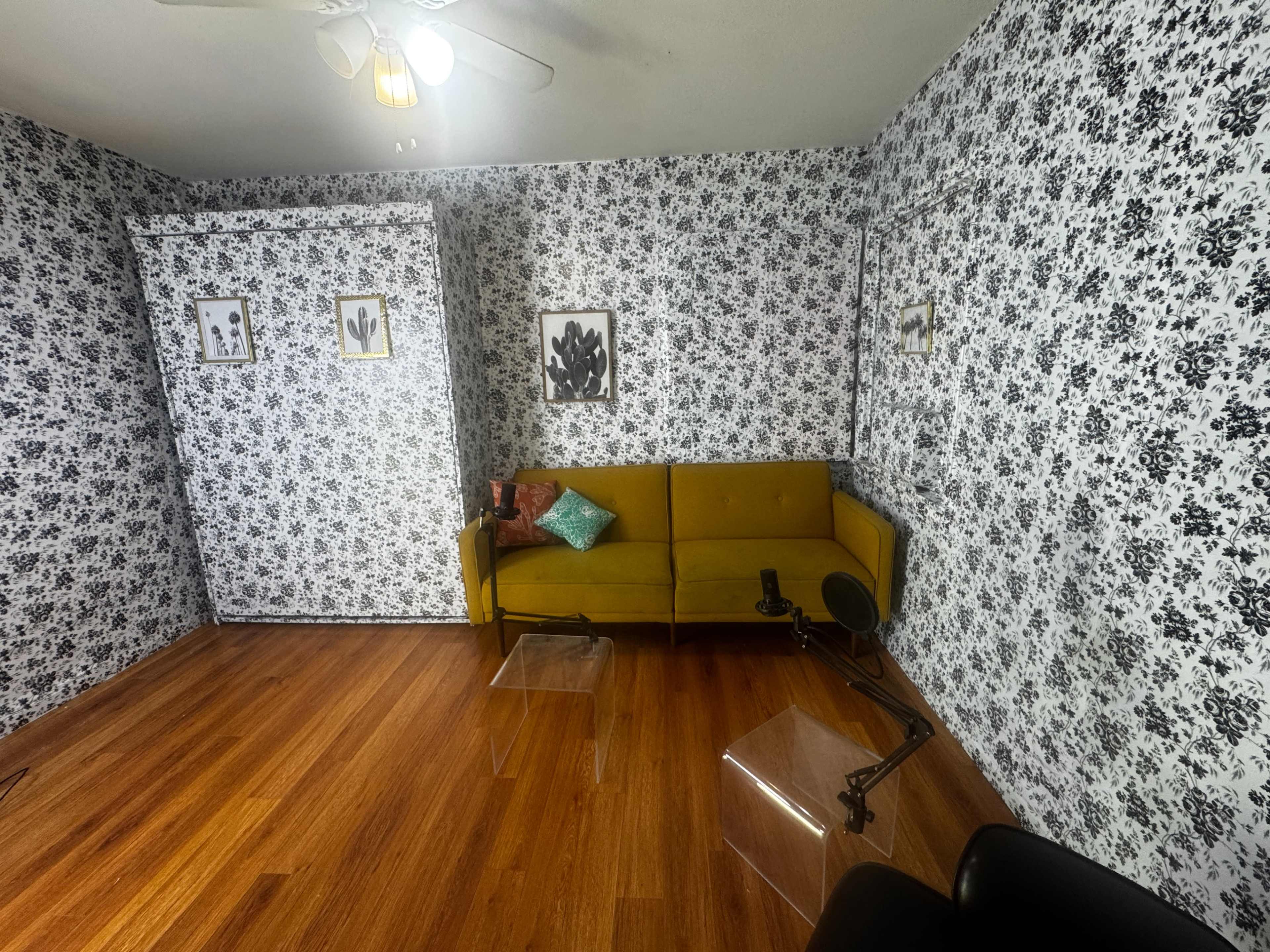 The image shows a room with a yellow couch, a clear acrylic coffee table, and patterned black and white wallpaper.