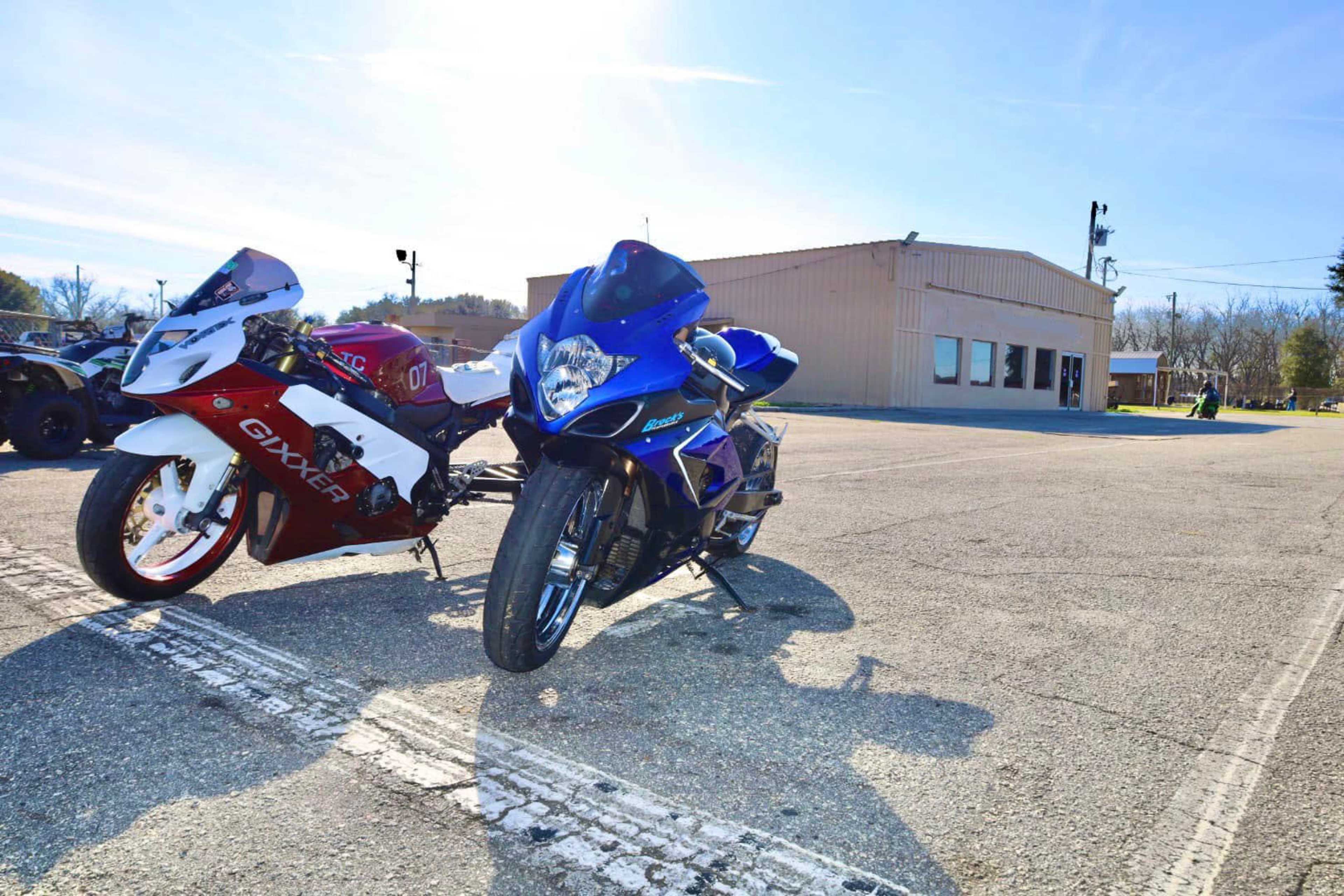 Two sport motorcycles, one red and white and the other blue, are parked on a paved lot beside a beige building.