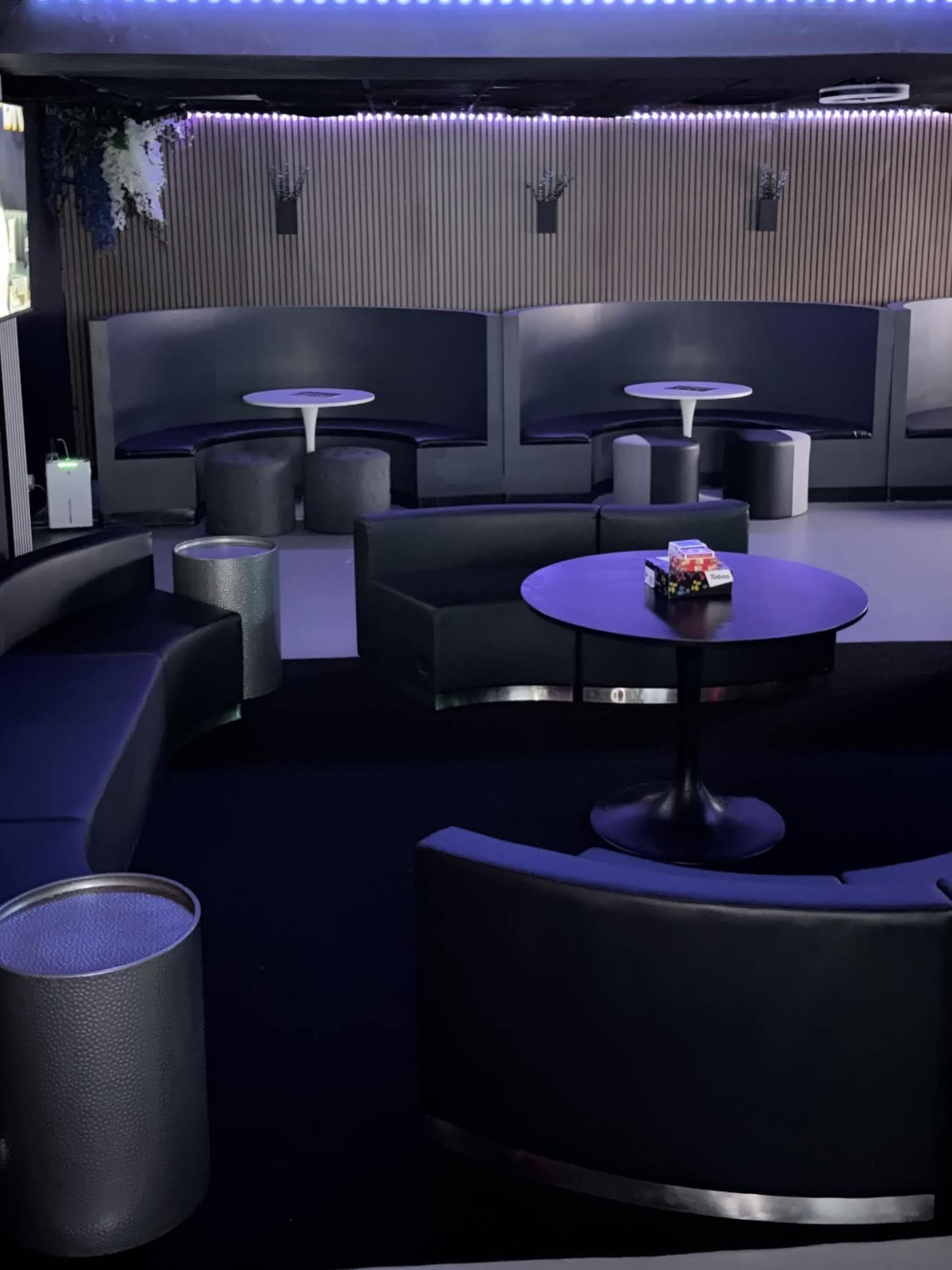 The image shows a modern lounge area with black curved seating, small round tables, and ambient lighting.