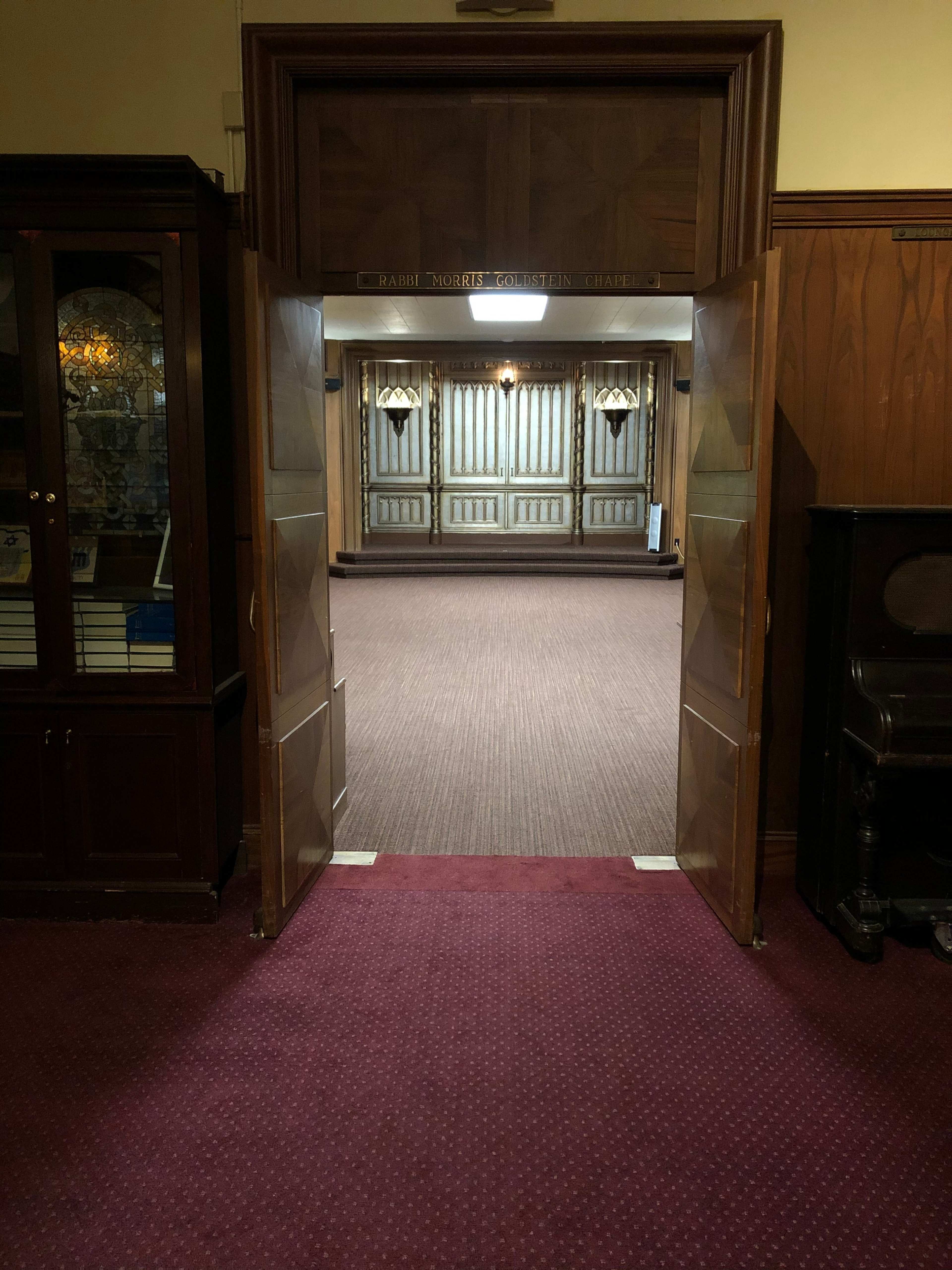 A pair of open wooden doors leads to a carpeted room with paneled walls and decorative fixtures.