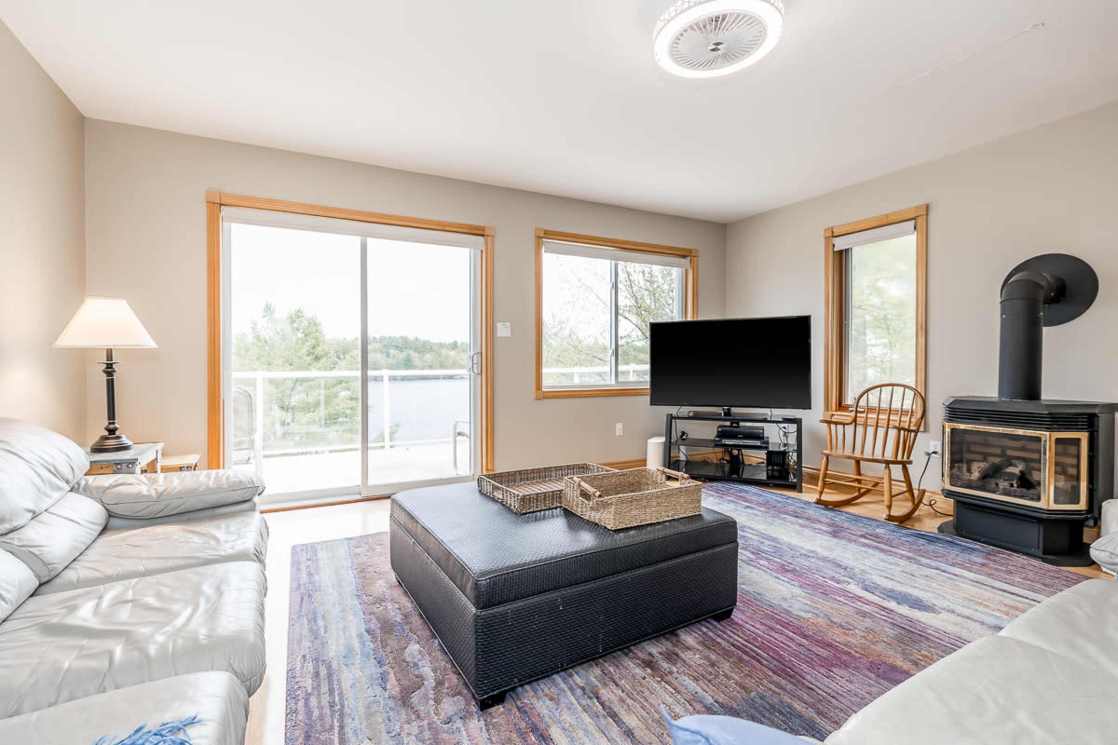 The living room features a large window with a view of the water, a sectional sofa, a coffee table, and a wood stove.