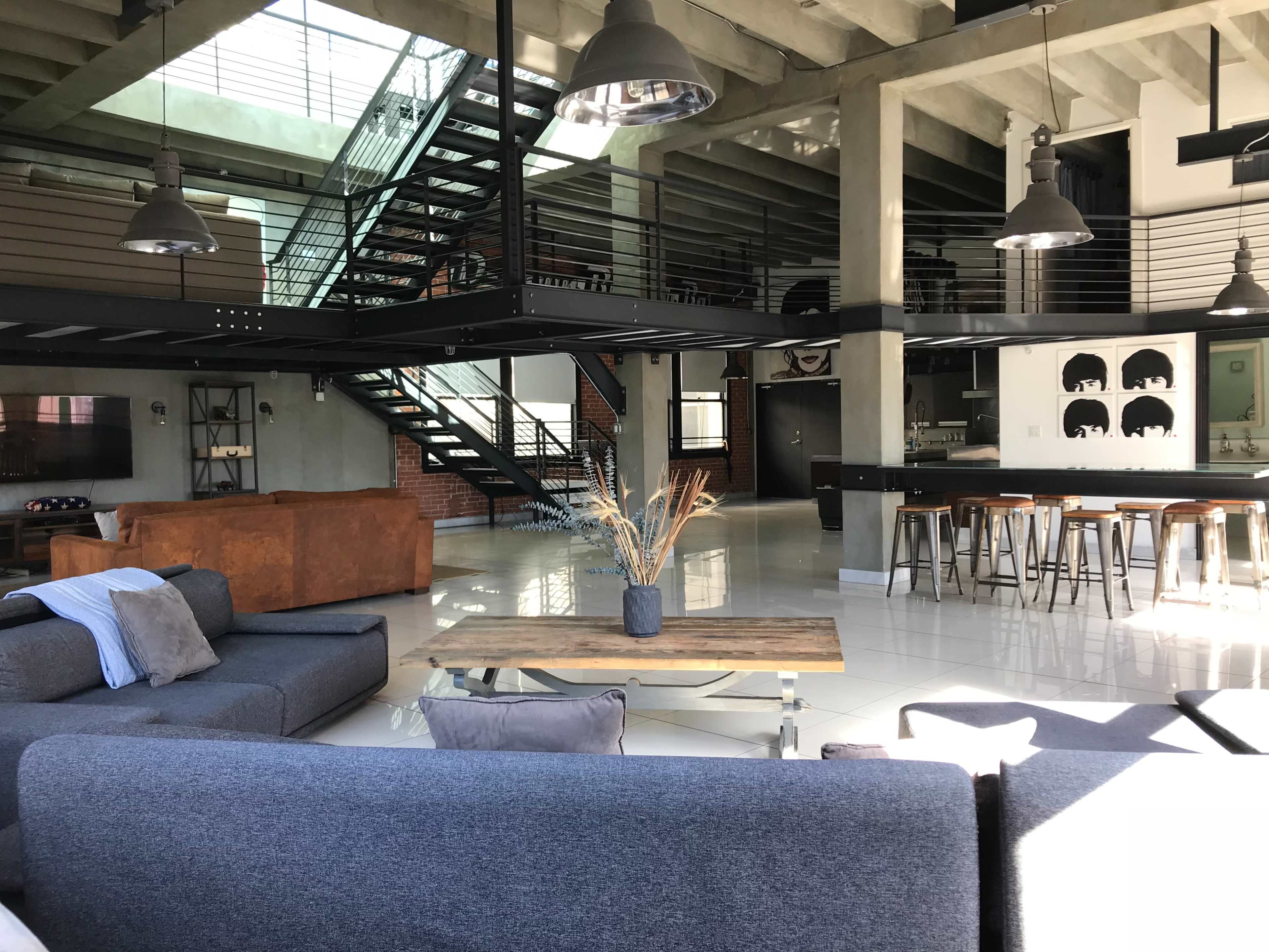 A modern, open-concept living space with a large seating area, sleek kitchen bar, and an upper-level staircase.