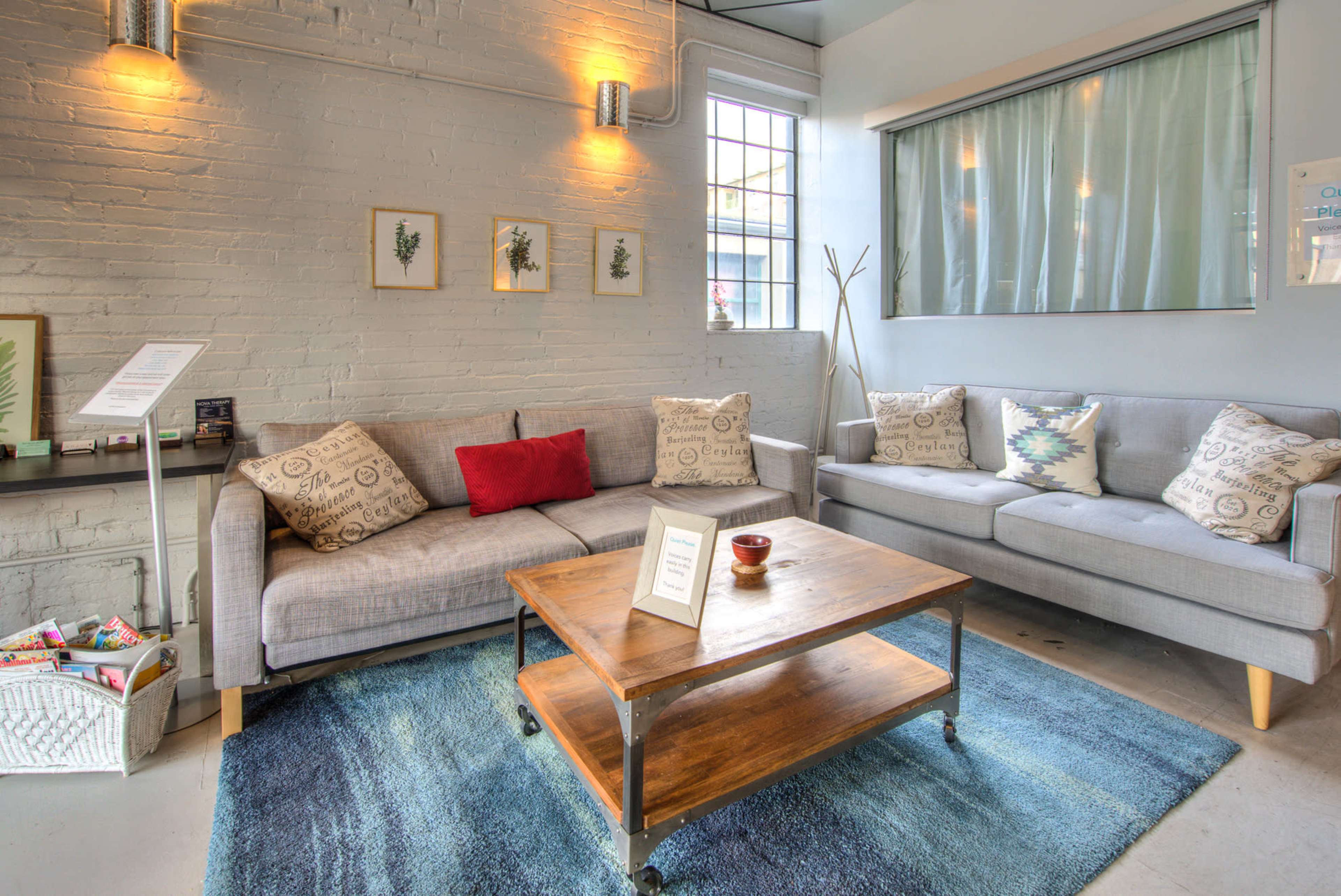 The scene shows a cozy sitting area with gray sofas, a wooden coffee table, and framed wall art, illuminated by ambient lighting.