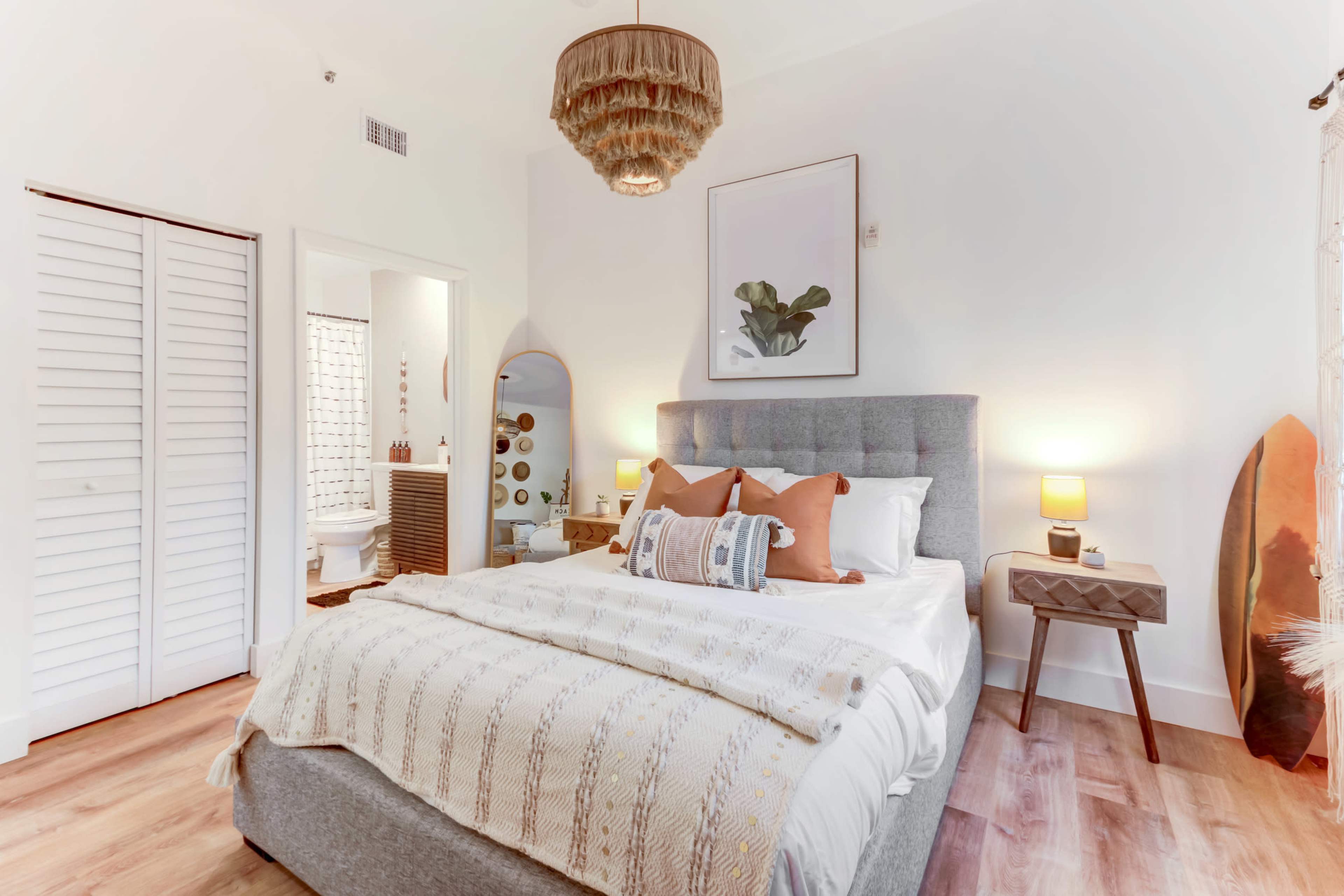 A neatly arranged bedroom featuring a gray upholstered bed, wooden flooring, and a softly lit atmosphere with decorative elements.
