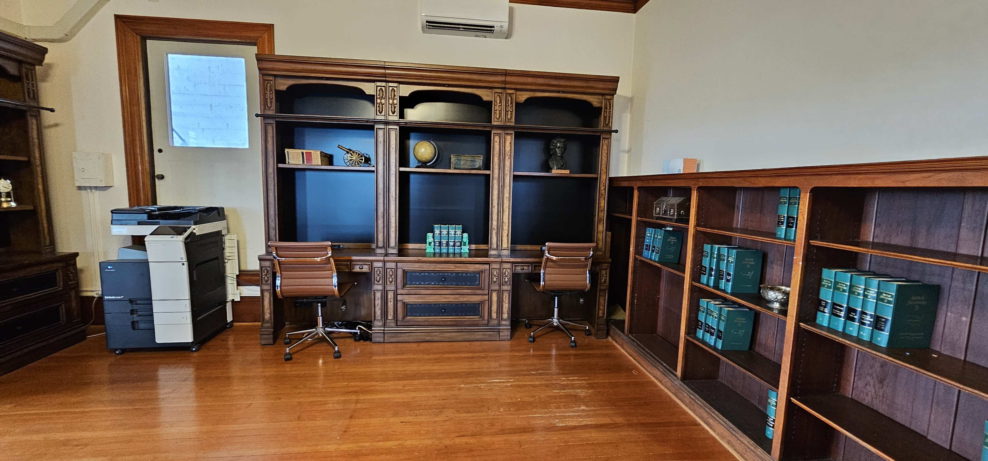 A spacious office with a wooden bookshelf, a desk area with two chairs, and a printer in the corner.
