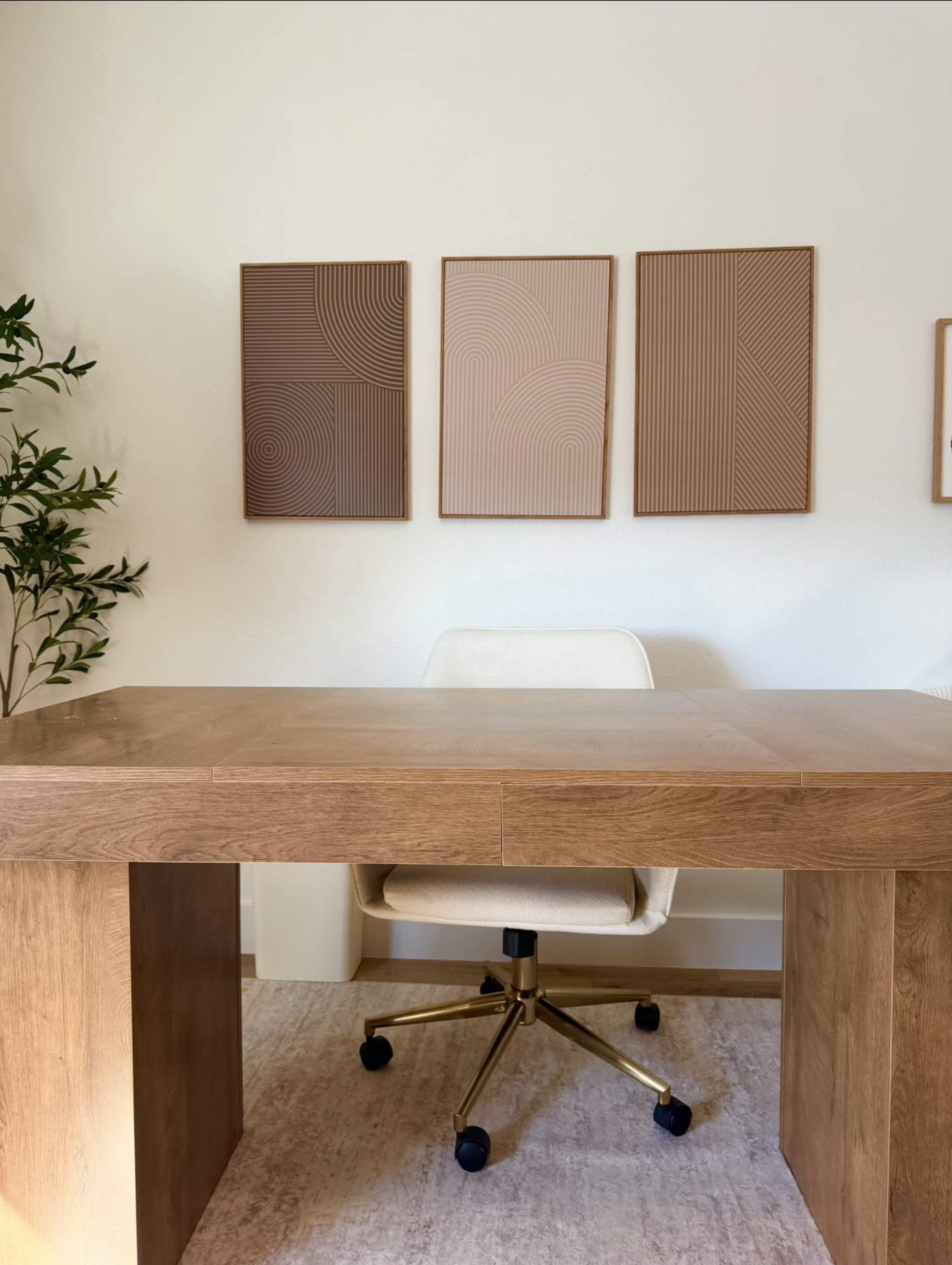 A wooden desk with a rolling chair is positioned in front of three geometric art pieces mounted on the wall.