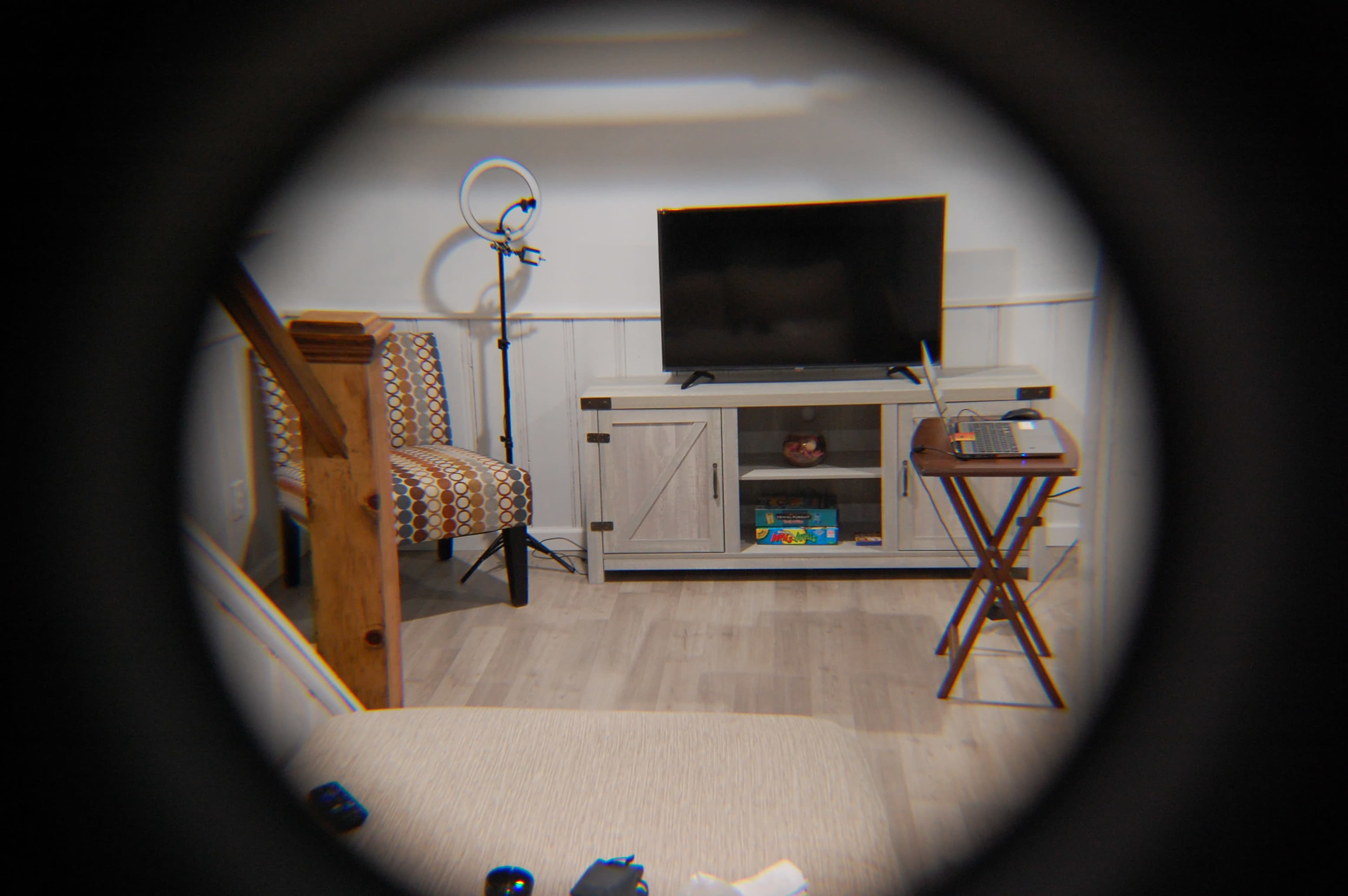 A living room scene features a television on a stand, a small table, a patterned chair, and a floor lamp.