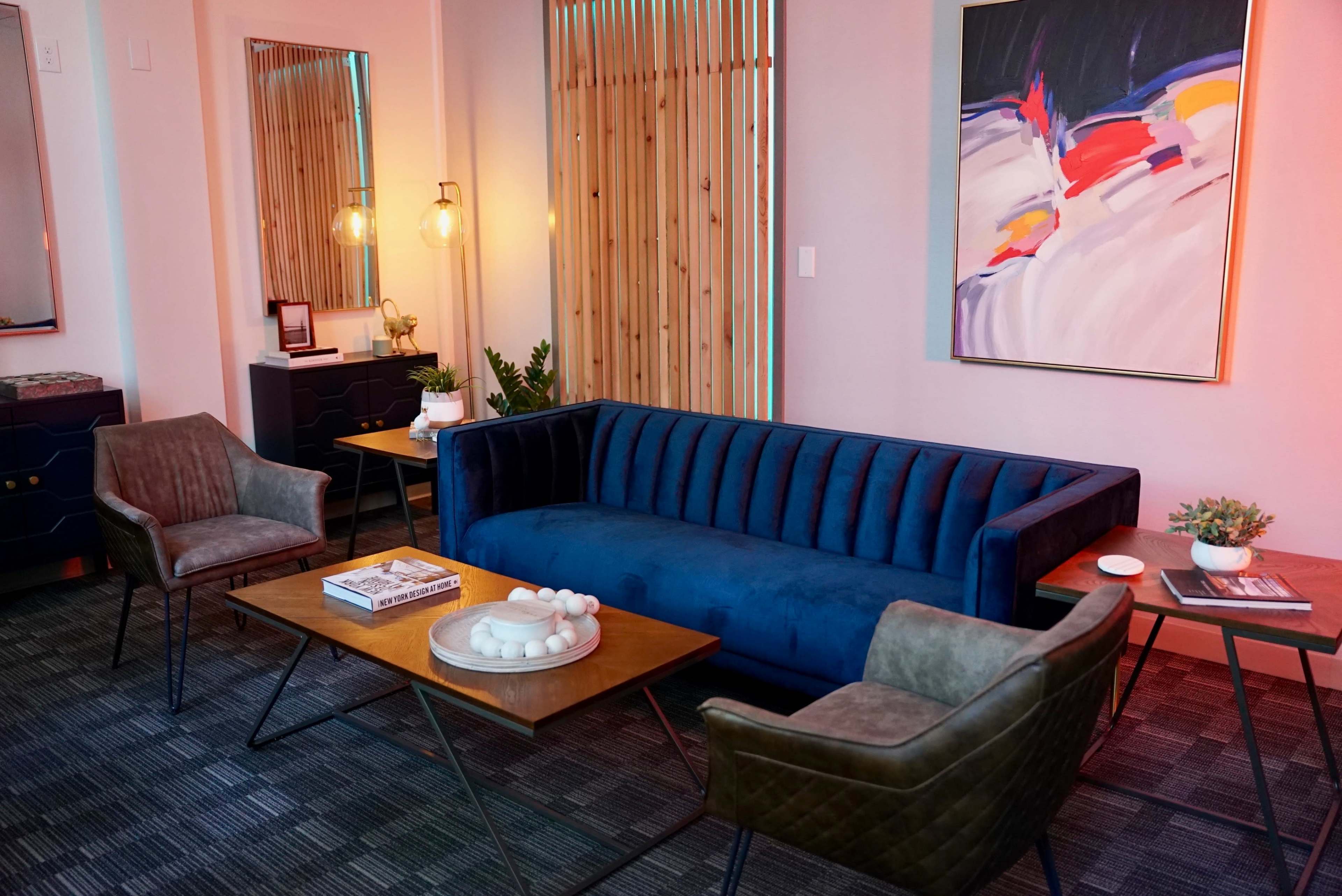 A modern living room with a blue velvet sofa, two stylish chairs, a wooden coffee table, and artwork on the wall.