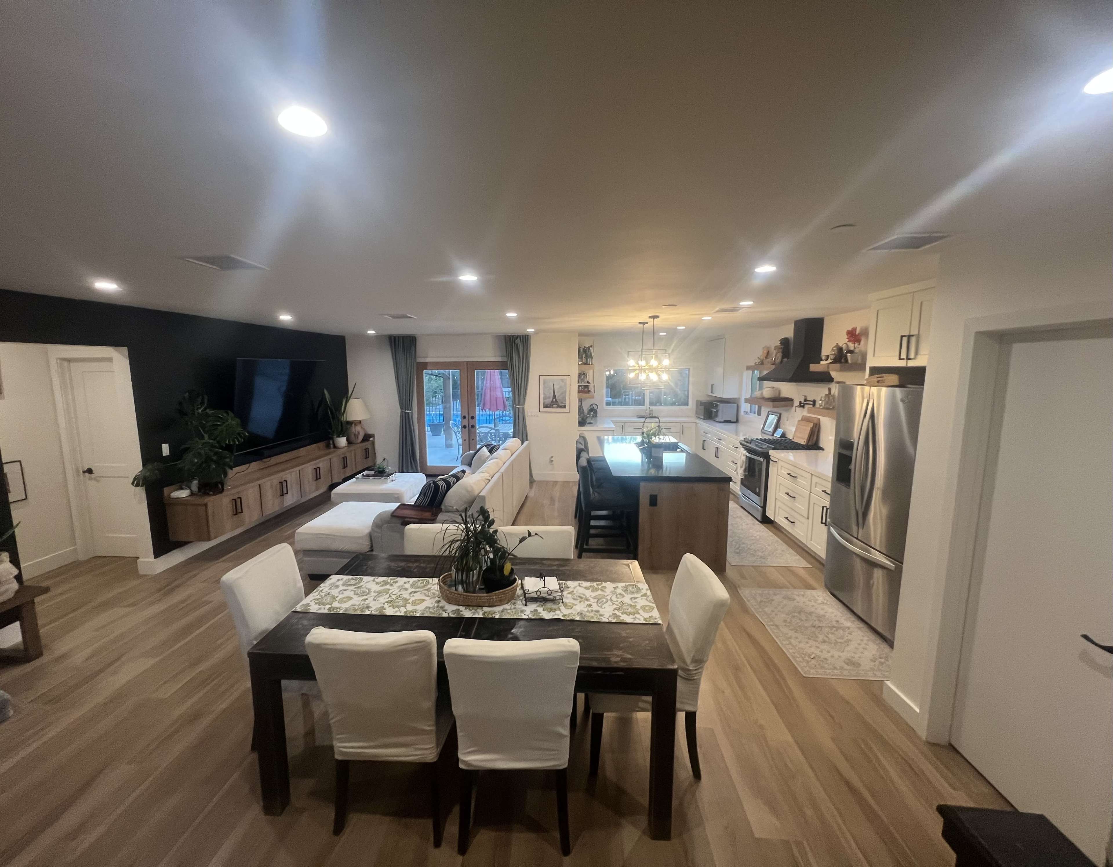 The image shows a modern open-concept living space featuring a dining area with a table and chairs, a kitchen with white cabinets, and a cozy seating area with a sofa.