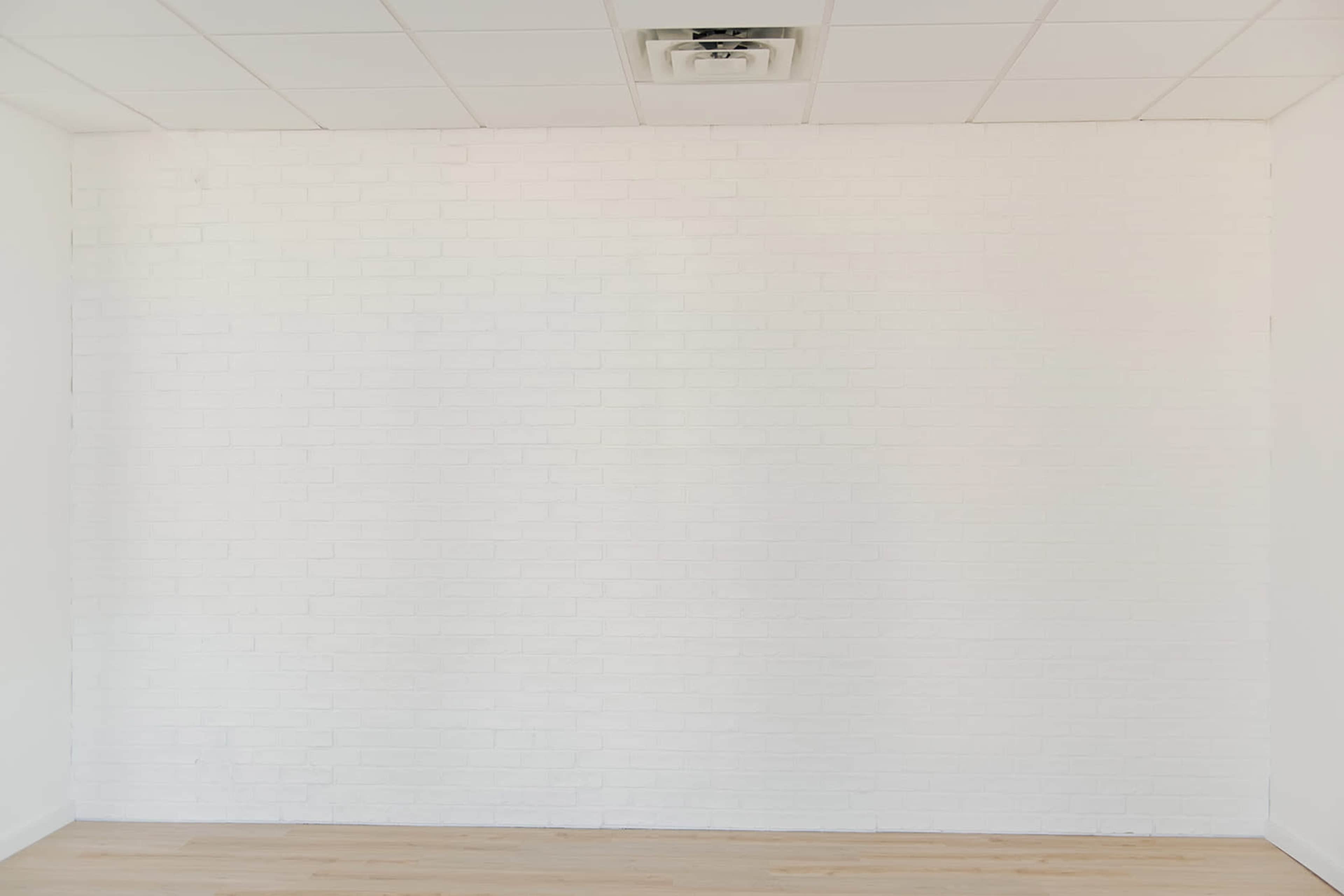 The image shows a blank white wall with a light wood floor and a ceiling with tiles.