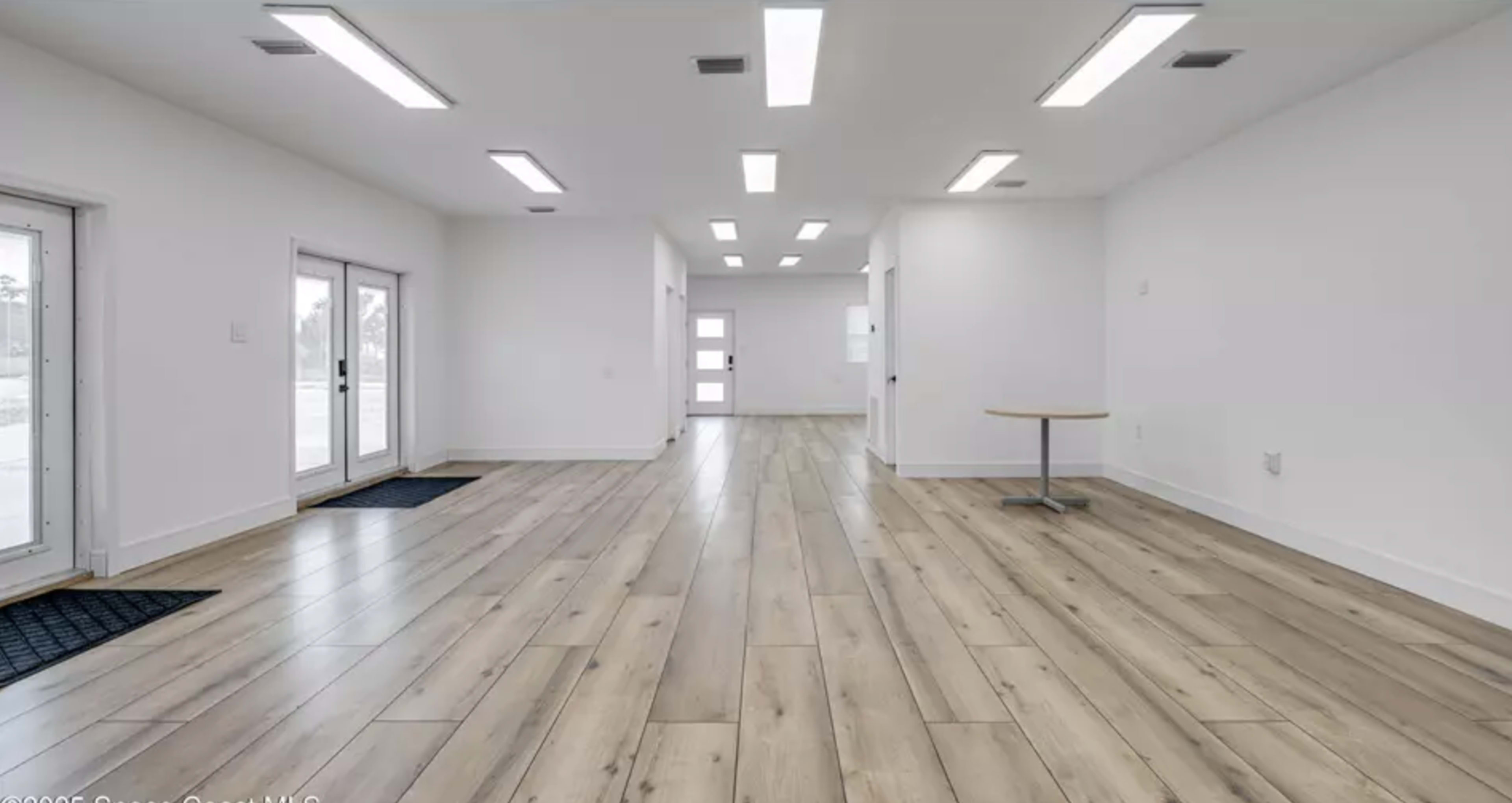 The image shows a spacious, well-lit interior with hardwood floors and several doorways leading to other rooms.