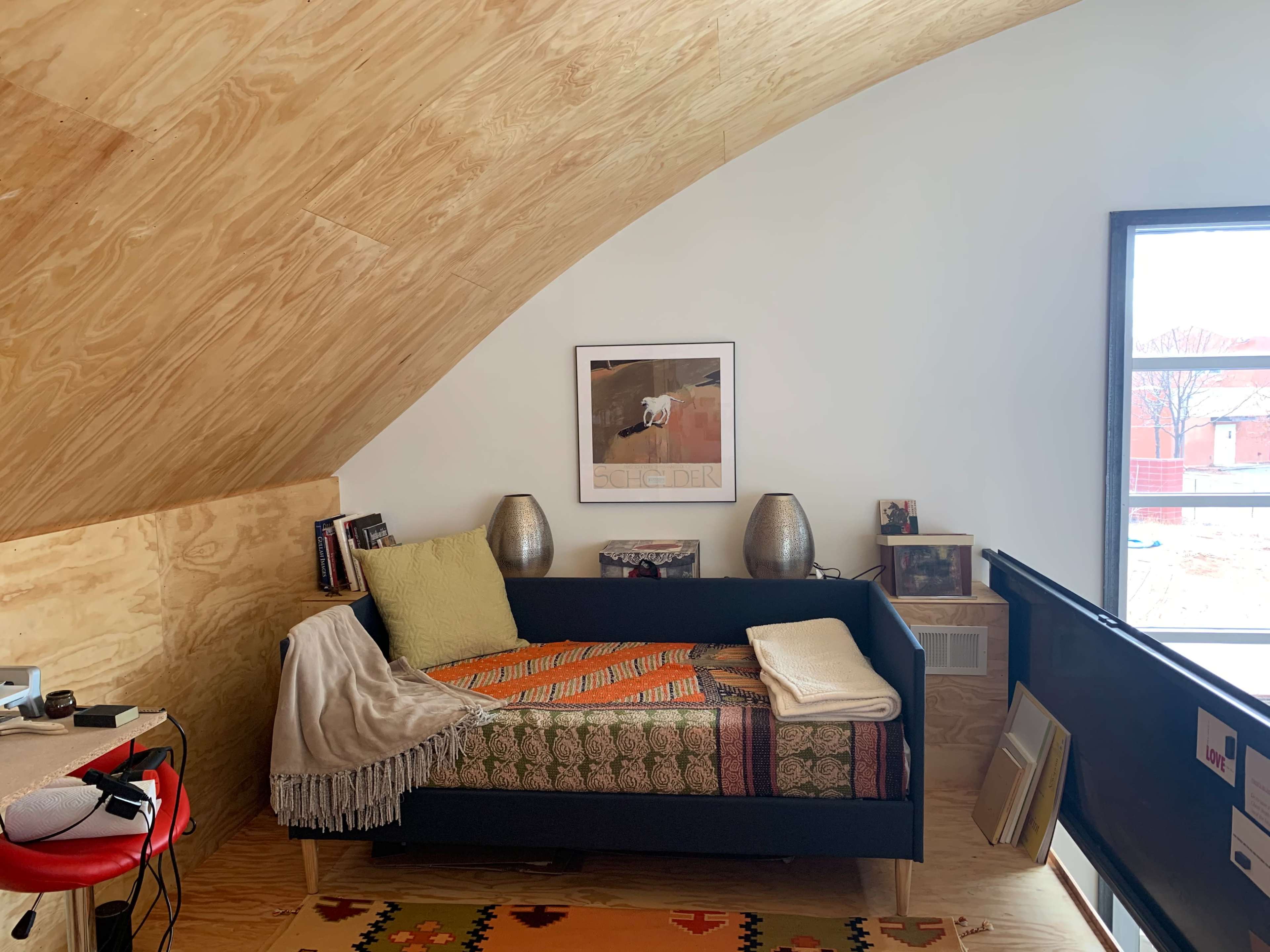 A cozy corner of a room with a dark blue couch covered in a patterned throw, accompanied by two metallic lamps and a framed picture on the wall.
