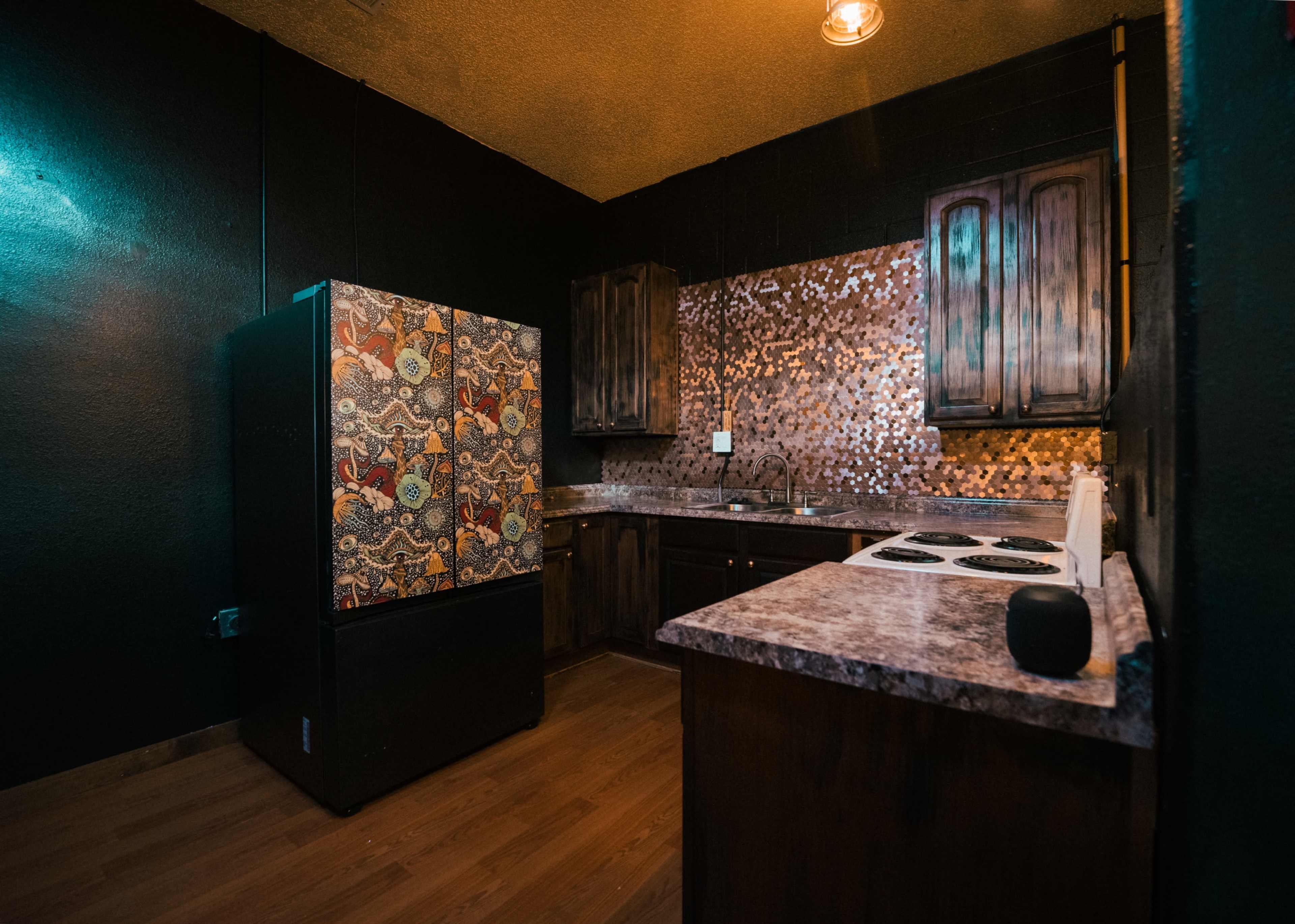 The image shows a kitchen with dark walls, a patterned refrigerator, wooden cabinets, and a countertop with a stove.