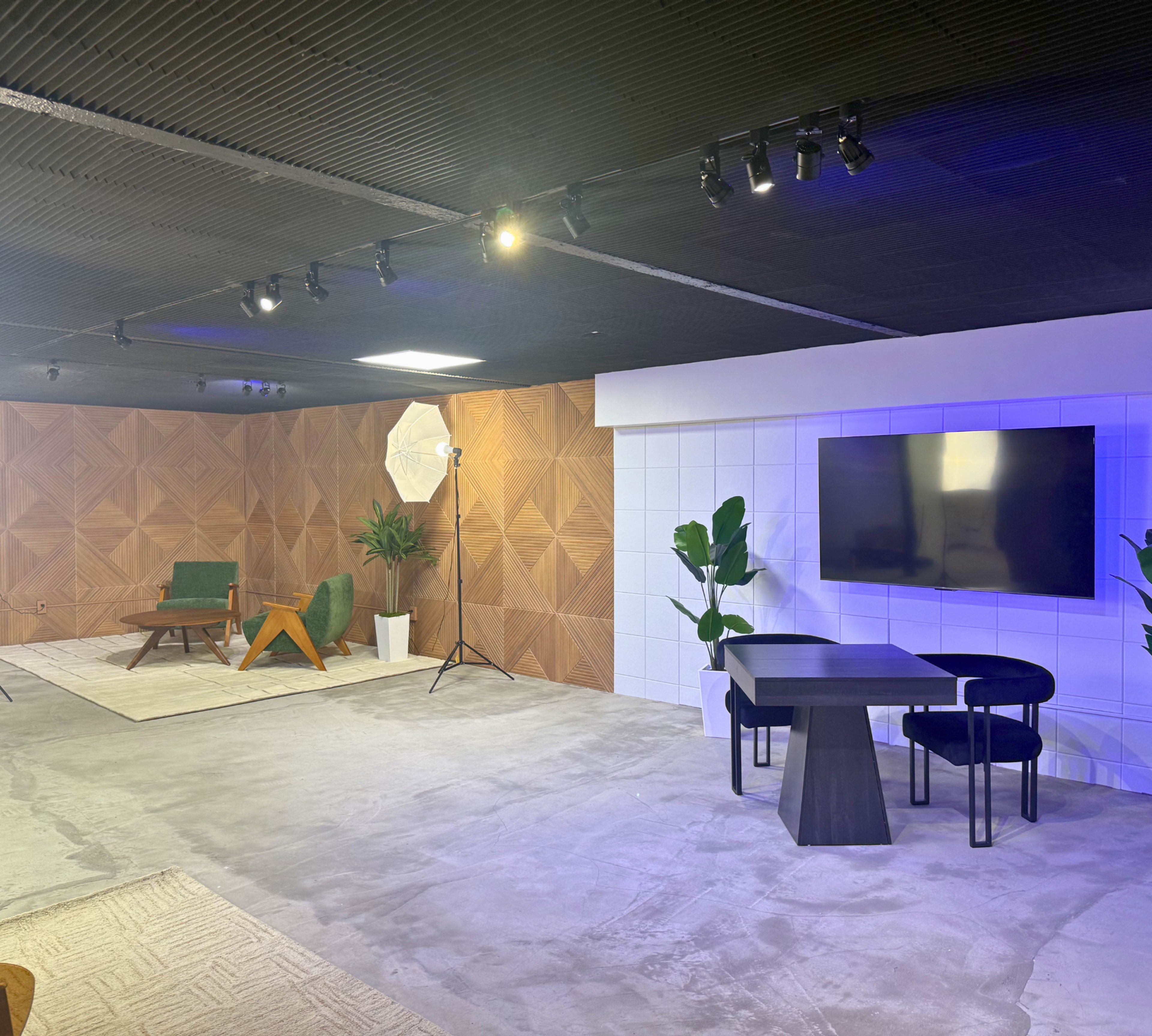 The image shows a modern interior space featuring a seating area with a green chair and a rug, a wall-mounted TV, and a table set up for meetings or discussions.