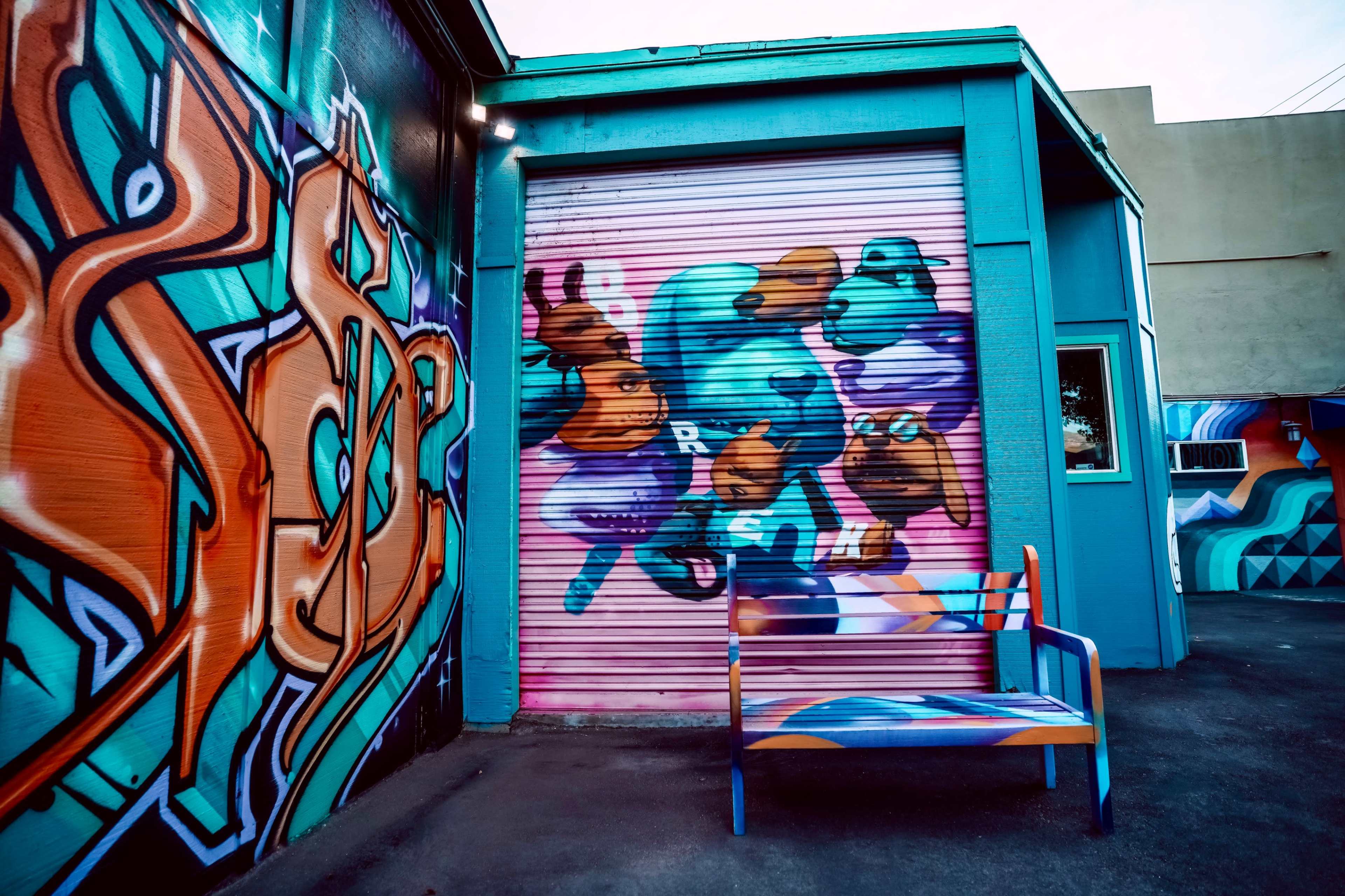 A colorful mural on a building featuring various animal faces alongside a stylized bench painted in vibrant shades.