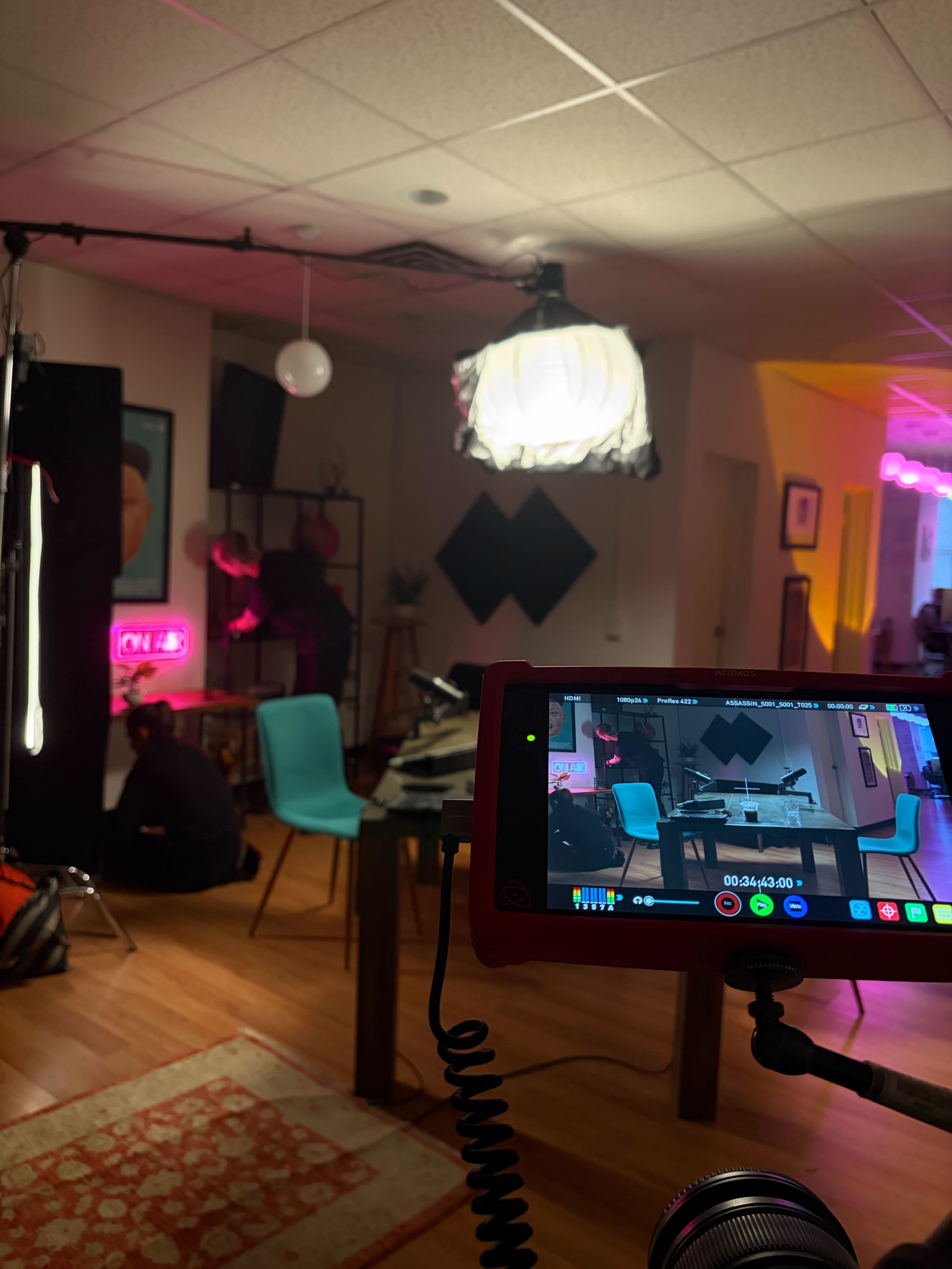 A camera is set up in a brightly lit room with neon signs, capturing a scene where a person is adjusting props on a shelf.