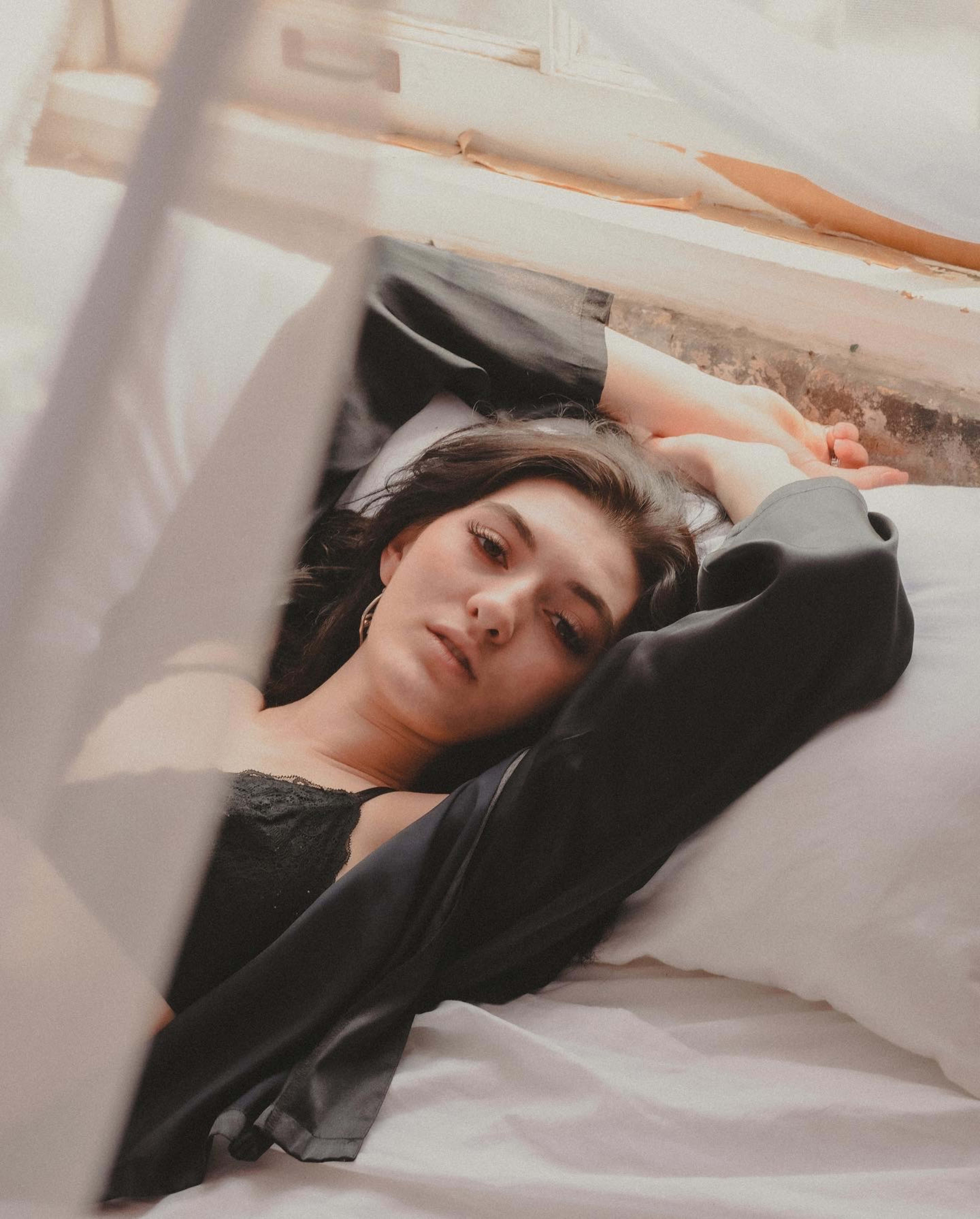 A woman posing on a white bed during a boudoir photo shoot.