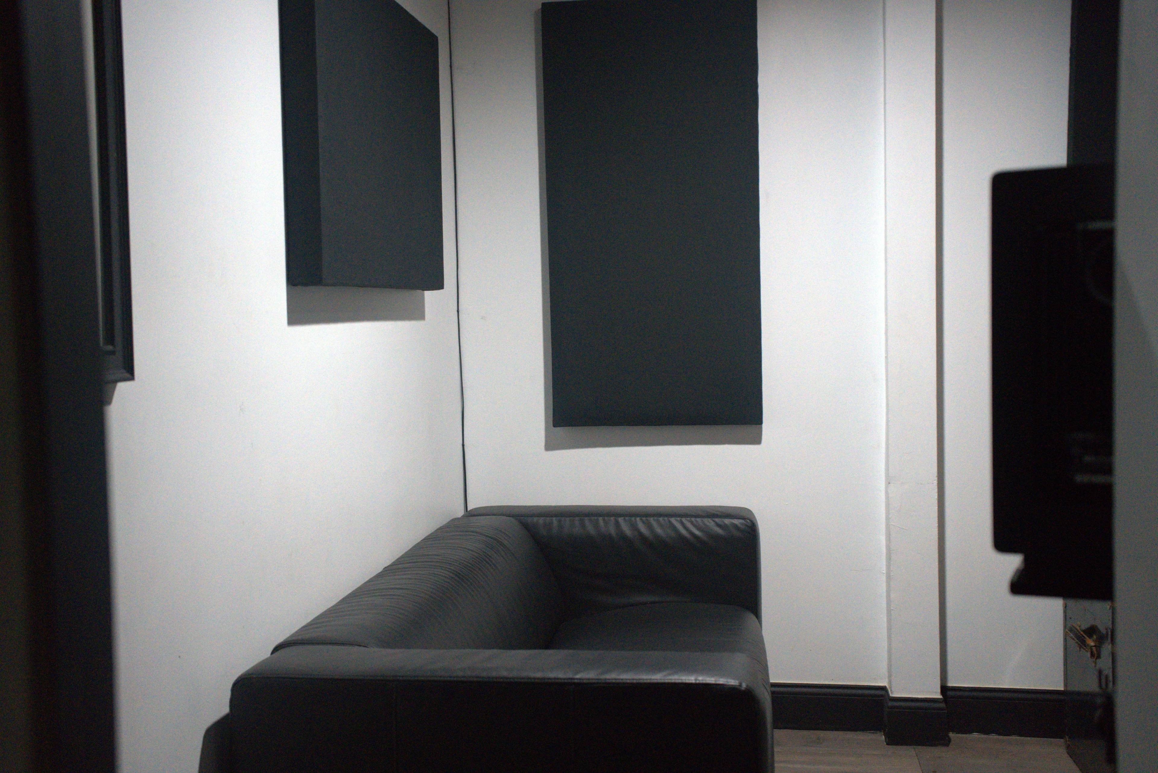 A small room with a black leather couch and two soundproofing panels mounted on the wall.