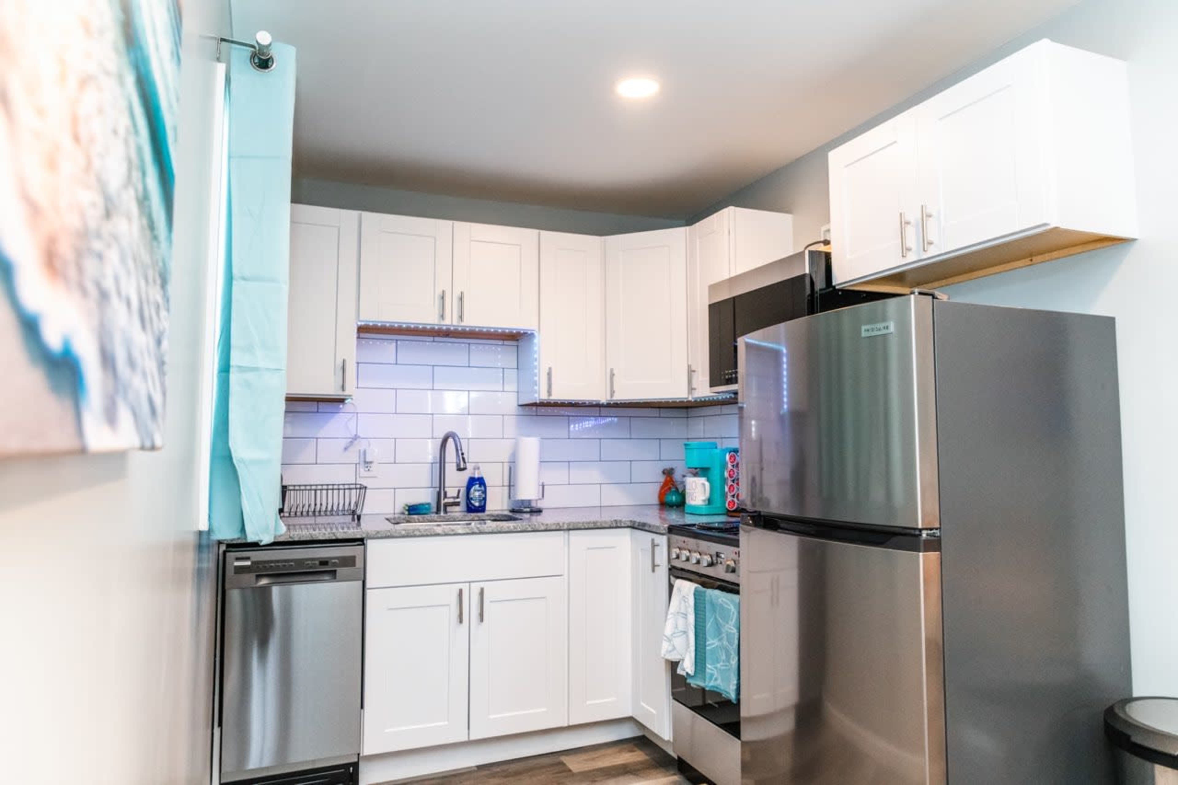 A compact kitchen features white cabinets, stainless steel appliances, and a granite countertop with a contemporary backsplash.
