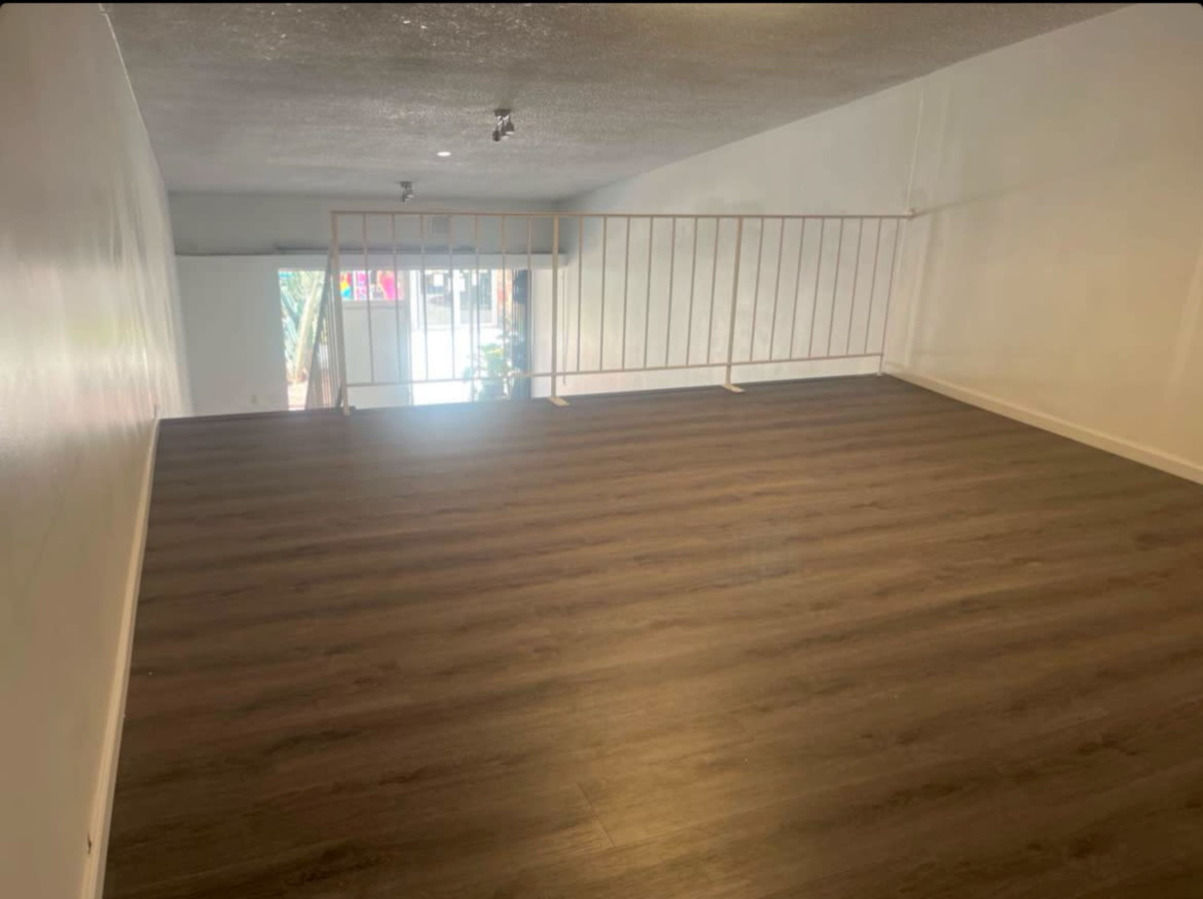 The image shows a spacious room with a wooden floor, featuring a railing and large windows that provide natural light.