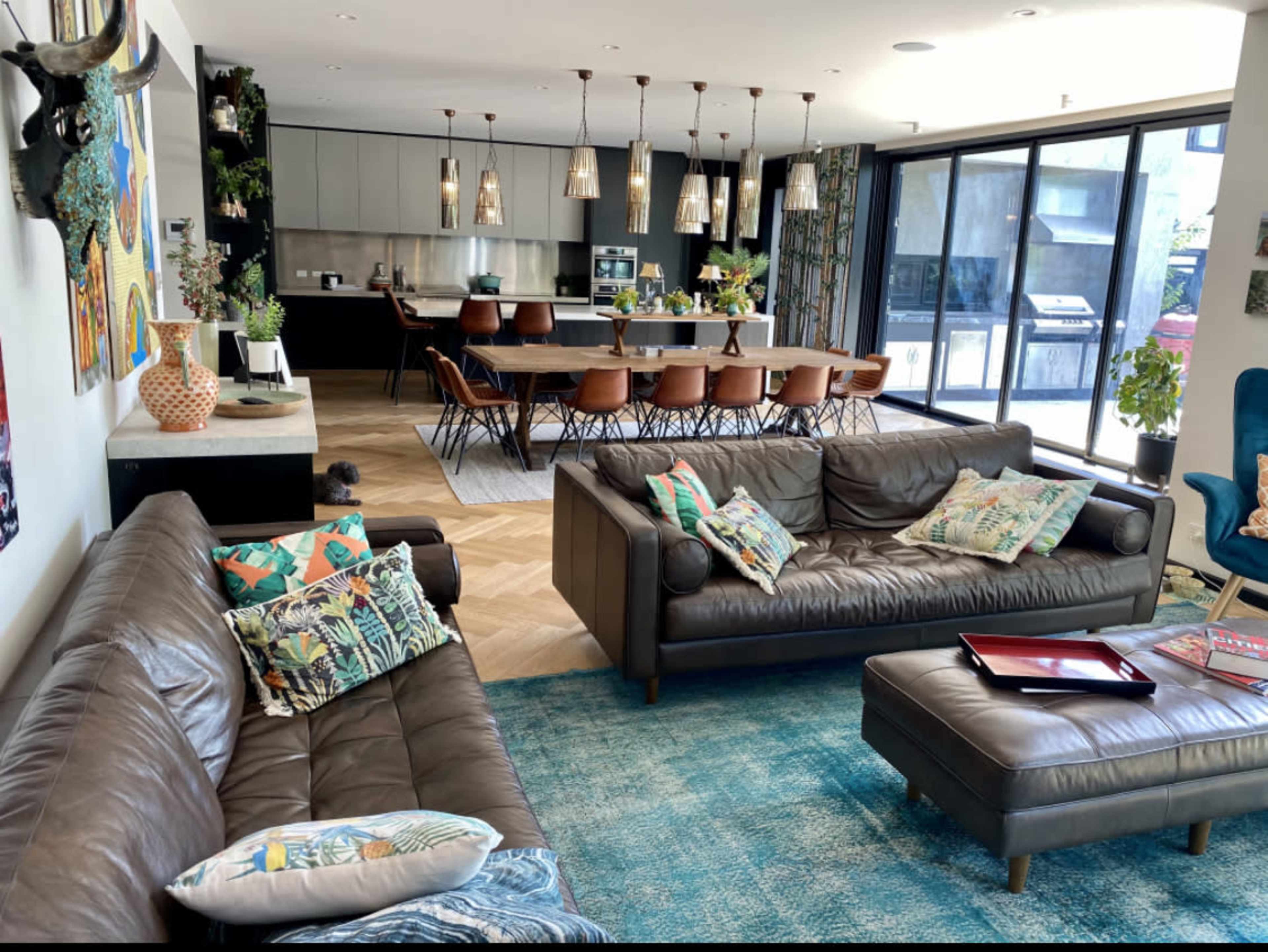 The image shows a modern open-concept living area with two leather sofas, a large dining table, and a sleek kitchen in the background.