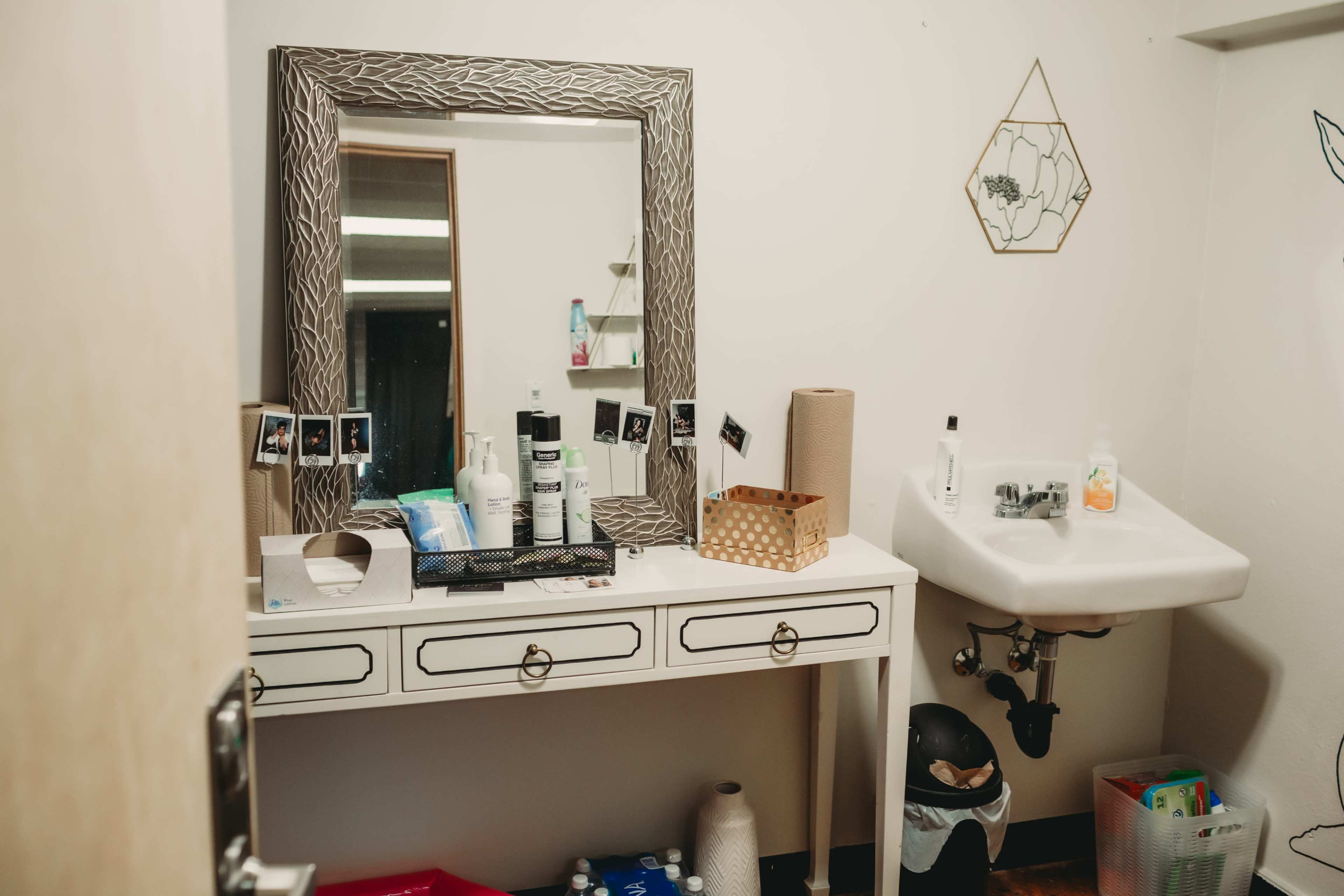 A bathroom counter displays various toiletries, a mirror with decorative edges, and a small sink nearby.