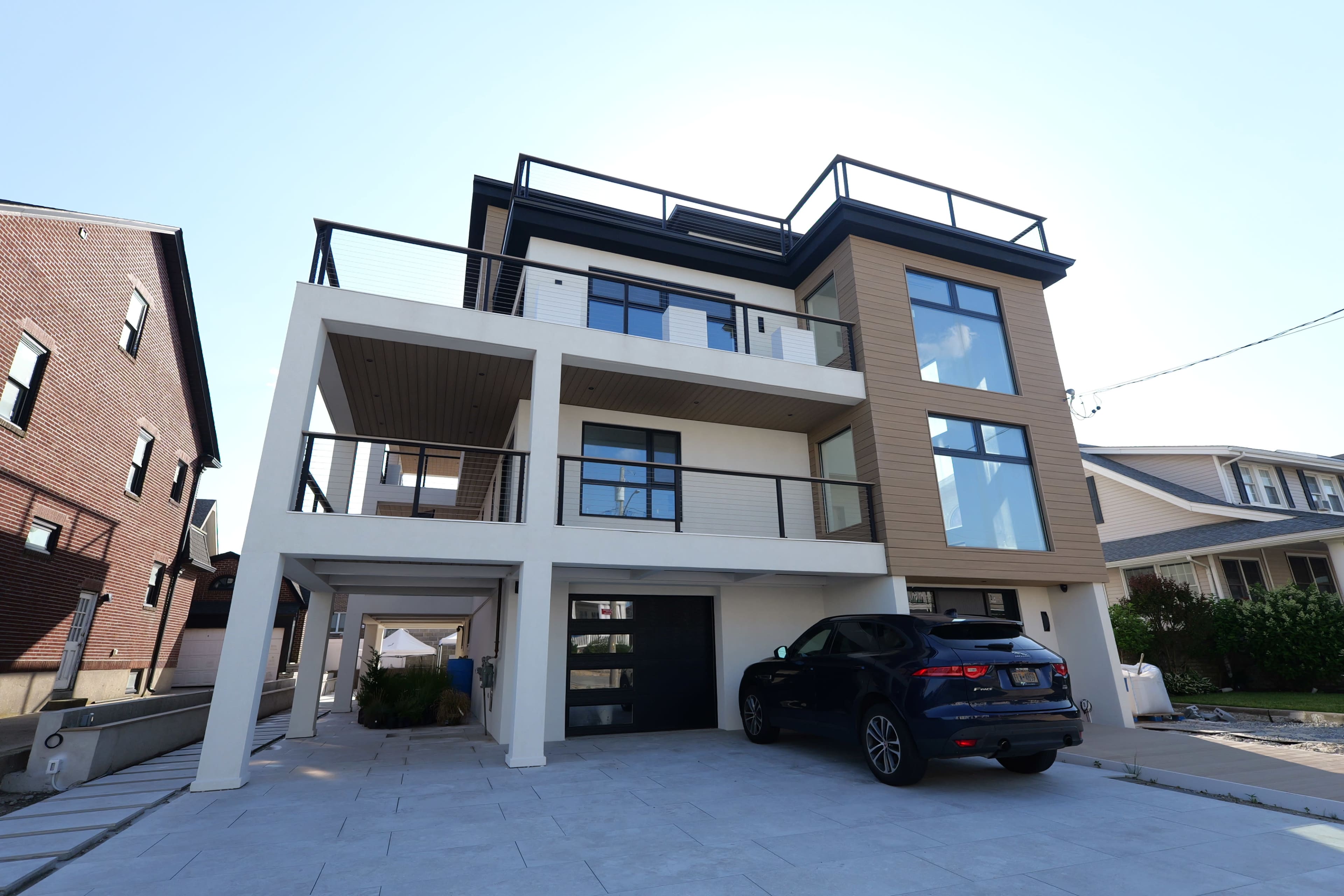 The image shows a modern multi-story house with a two-car garage and a black SUV parked in the driveway.