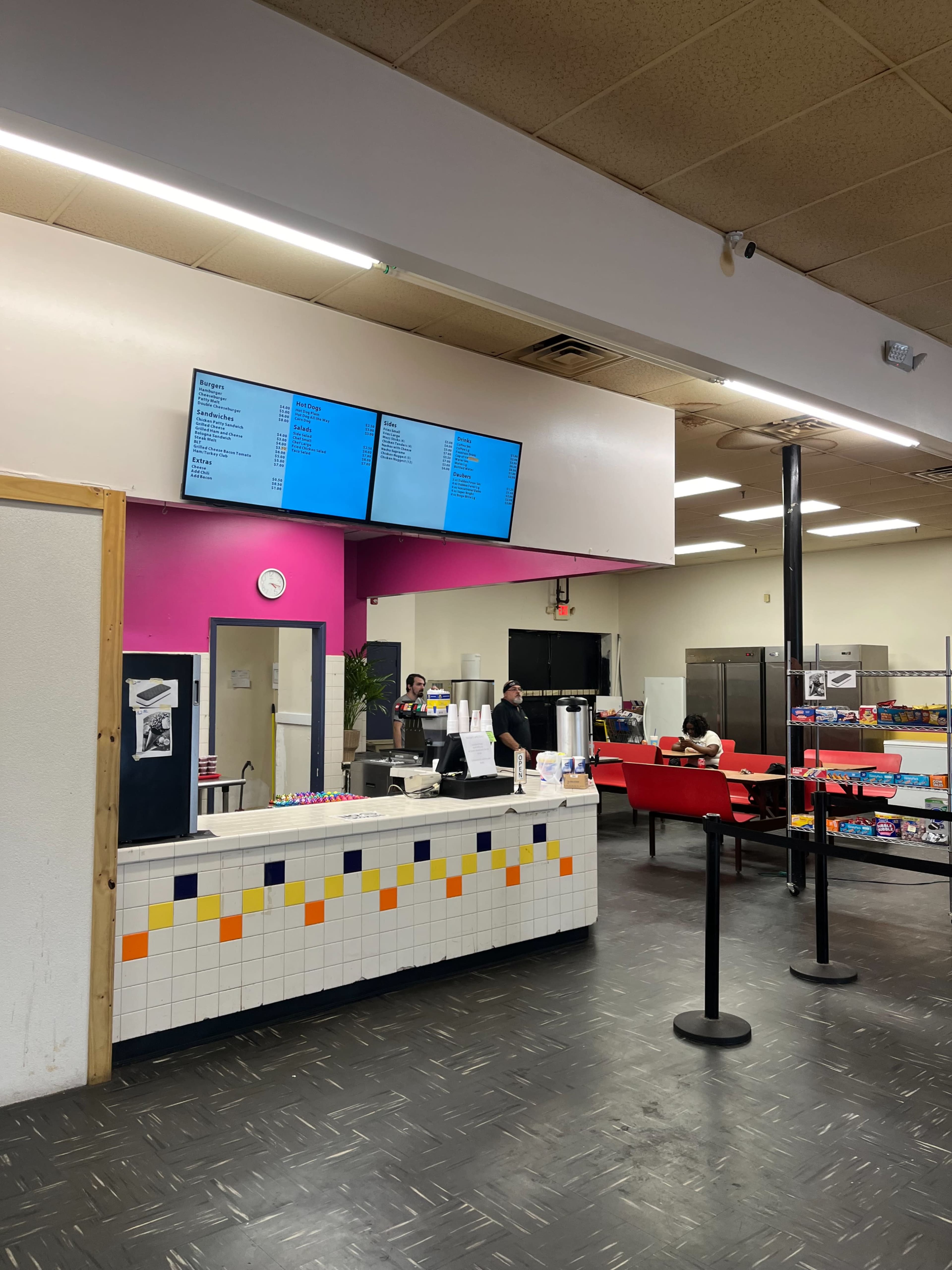 An interior of a food establishment featuring a service counter with a menu display and seating area.