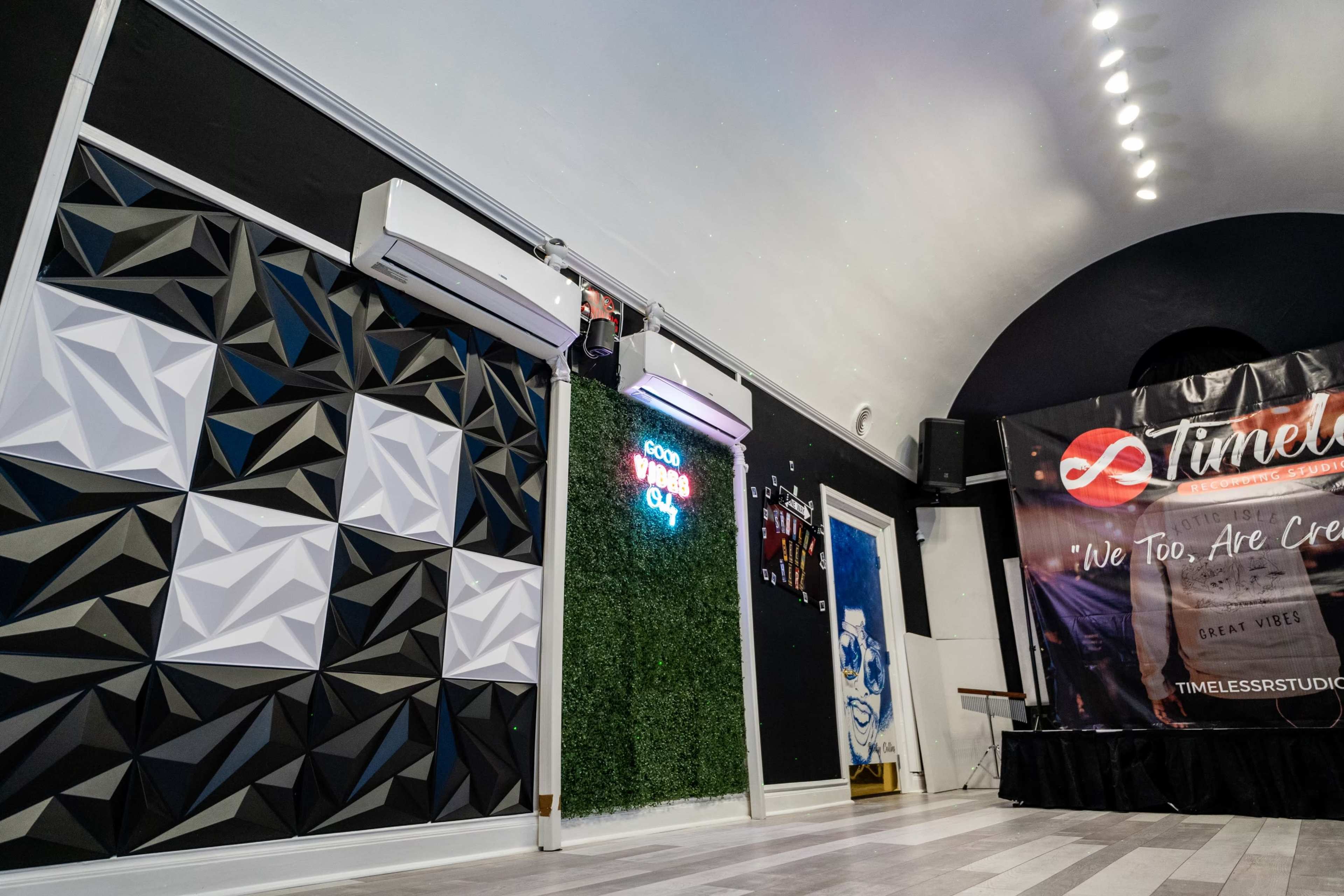 The image shows a modern interior space featuring a geometric wall panel, air conditioning units, neon signage, and a promotional banner.