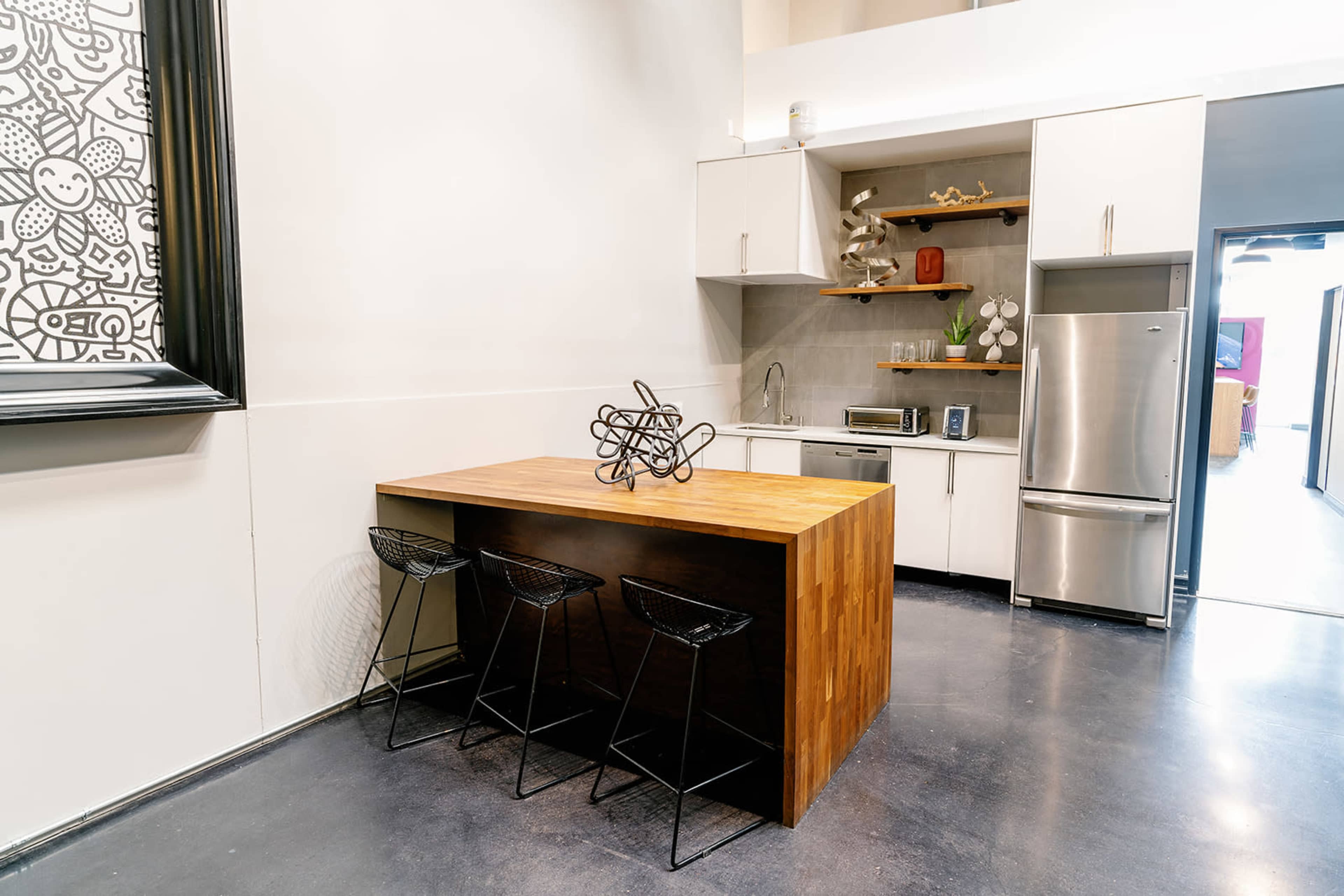 The image shows a modern kitchen with a wooden island and three black bar stools, featuring white cabinetry and stainless steel appliances.