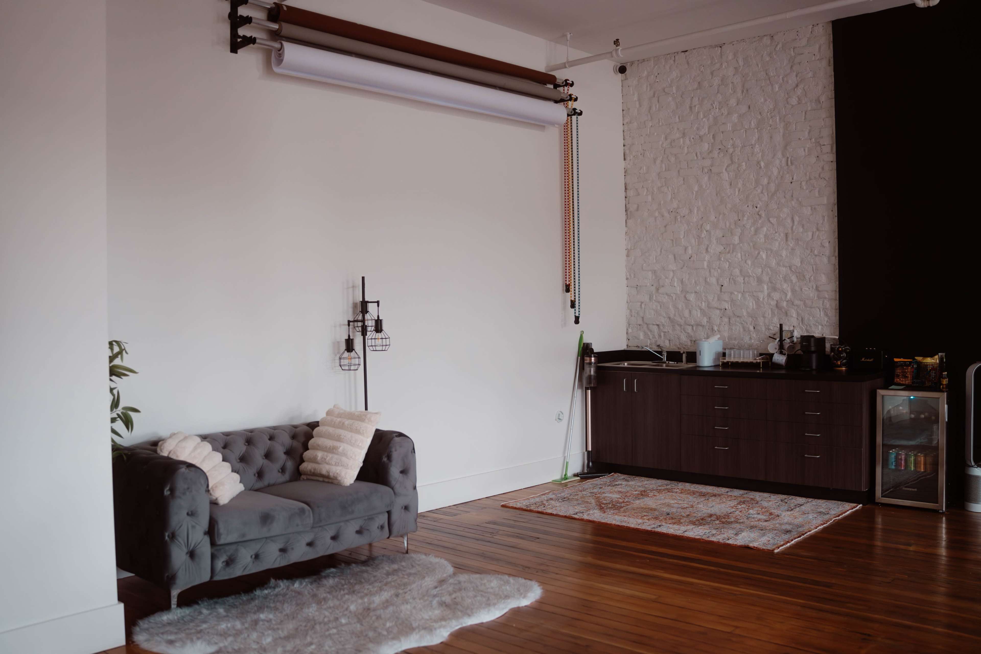 A modern interior features a tufted gray sofa, a small area rug, and a kitchenette against a textured wall.