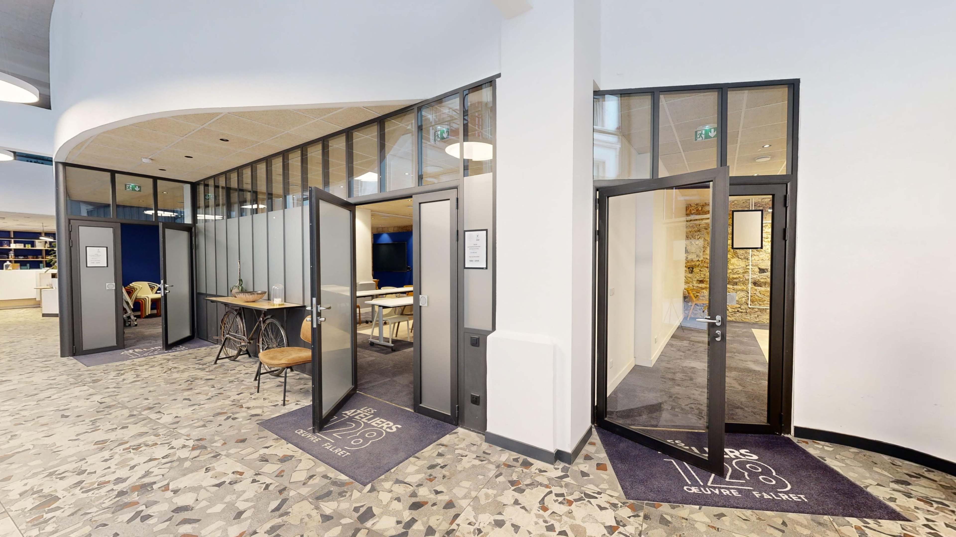 A modern hallway with multiple glass doors leading to meeting rooms, featuring a patterned floor and a reception area in the background.