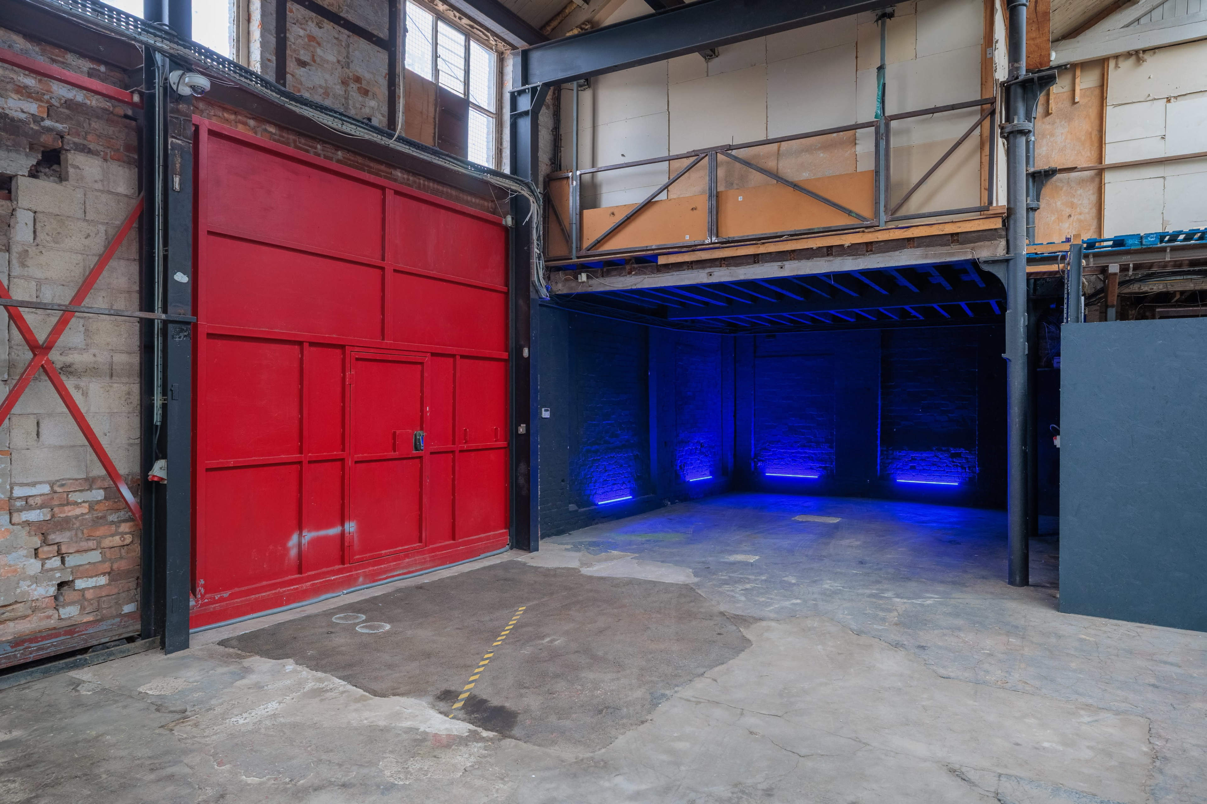 The image shows an industrial space with a red door on the left, blue lights illuminating the walls, and a concrete floor.